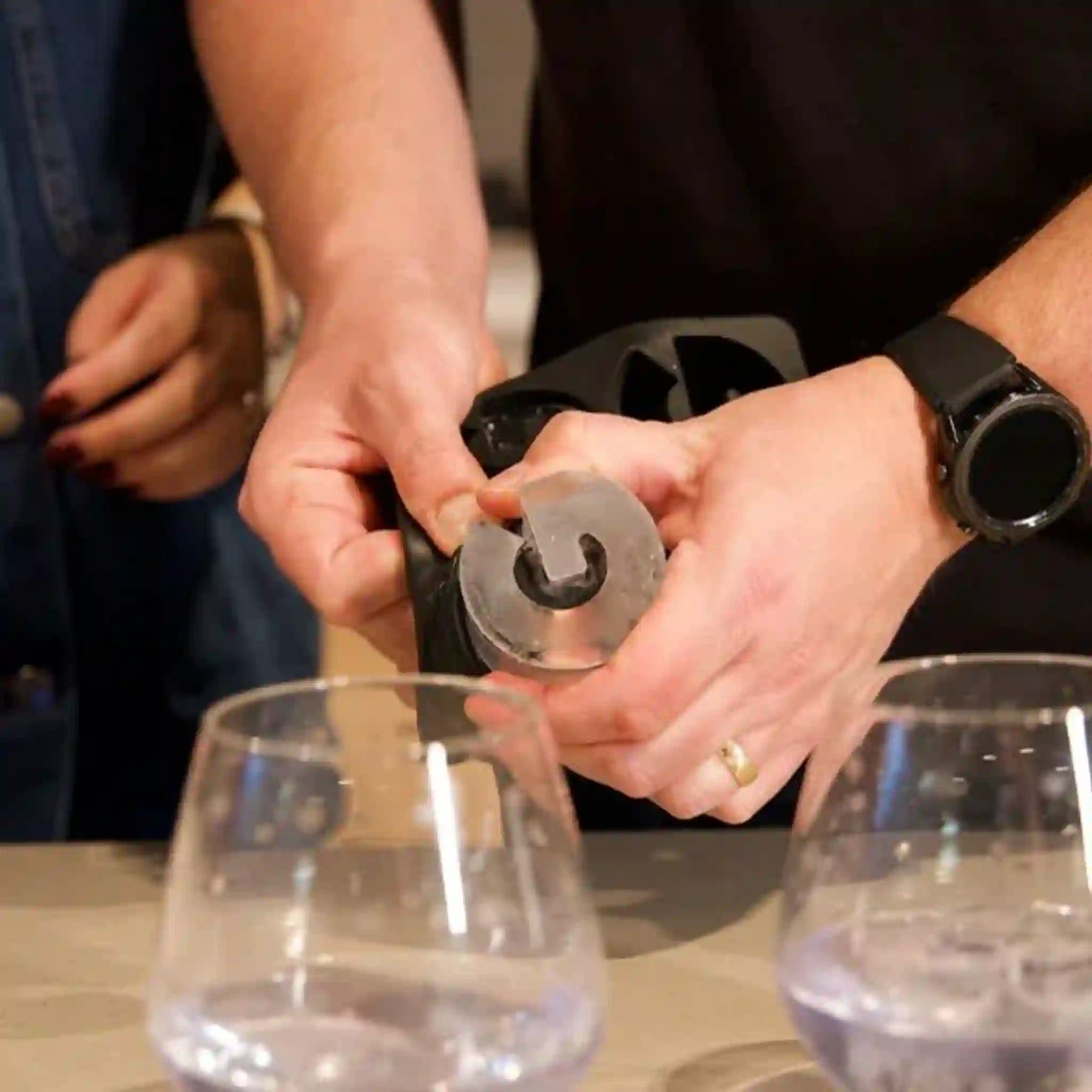Person using a wine bottle opener with two glasses on a table.