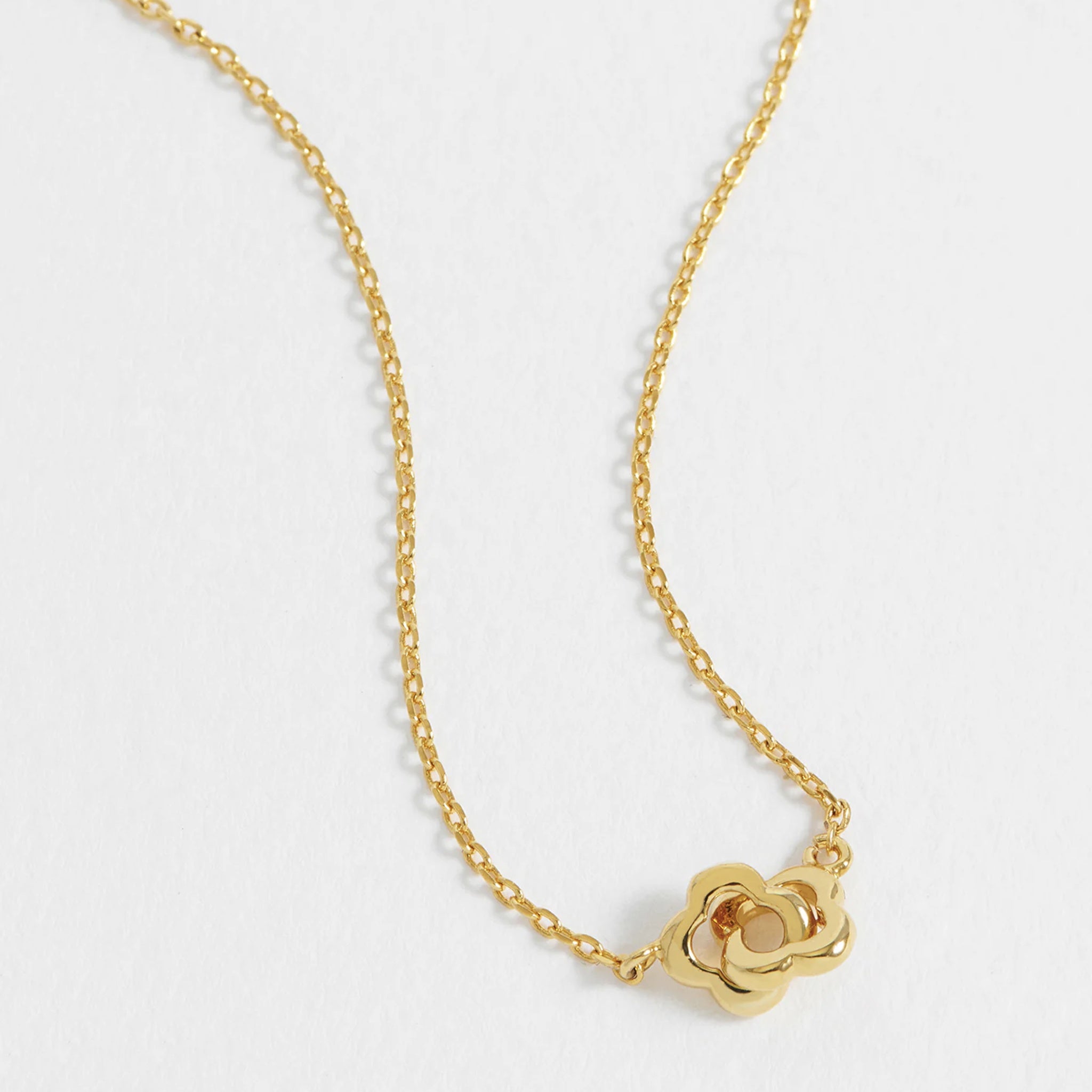 Gold necklace with a flower-shaped pendant on a light gray background