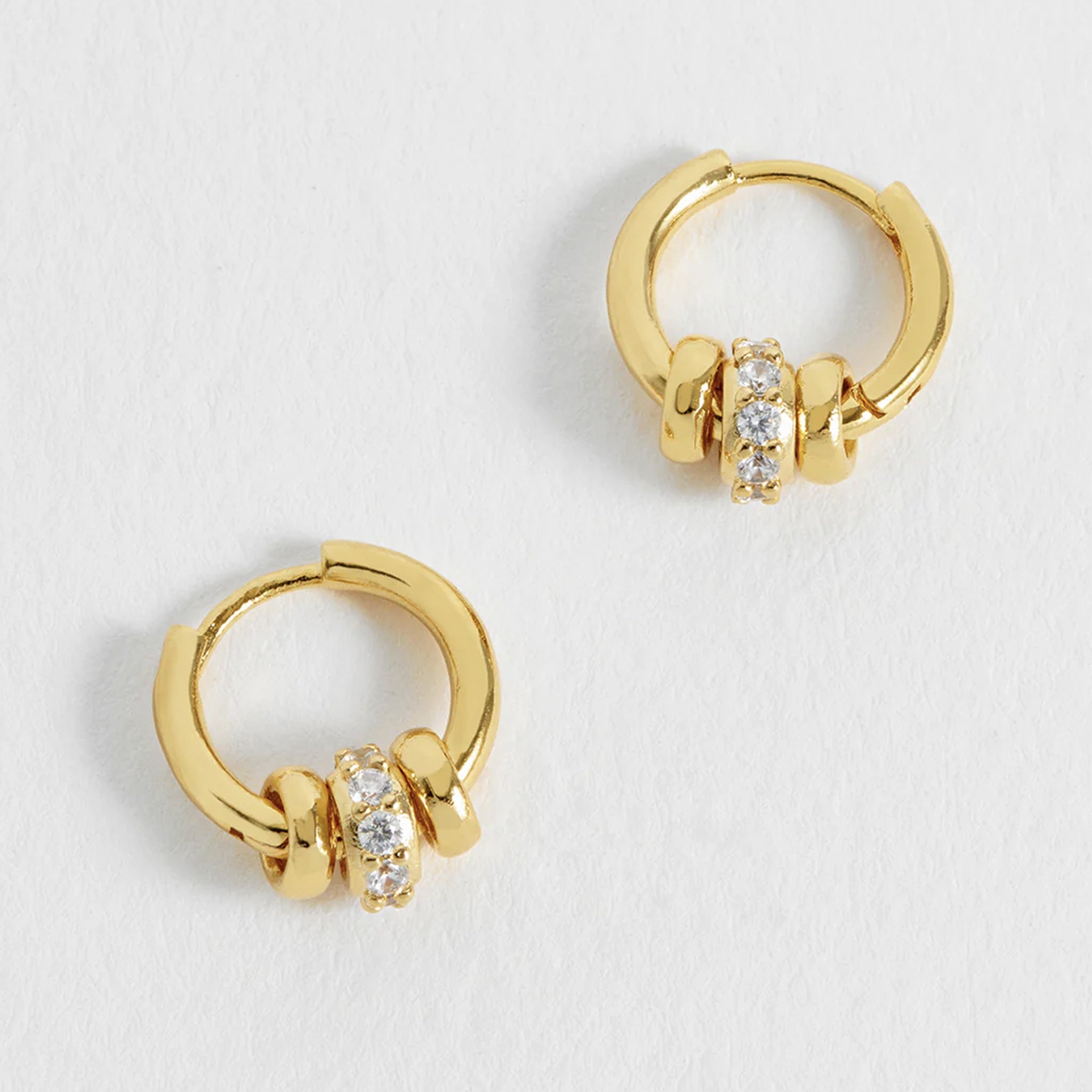 Gold hoop earrings with embedded stones on a light gray background