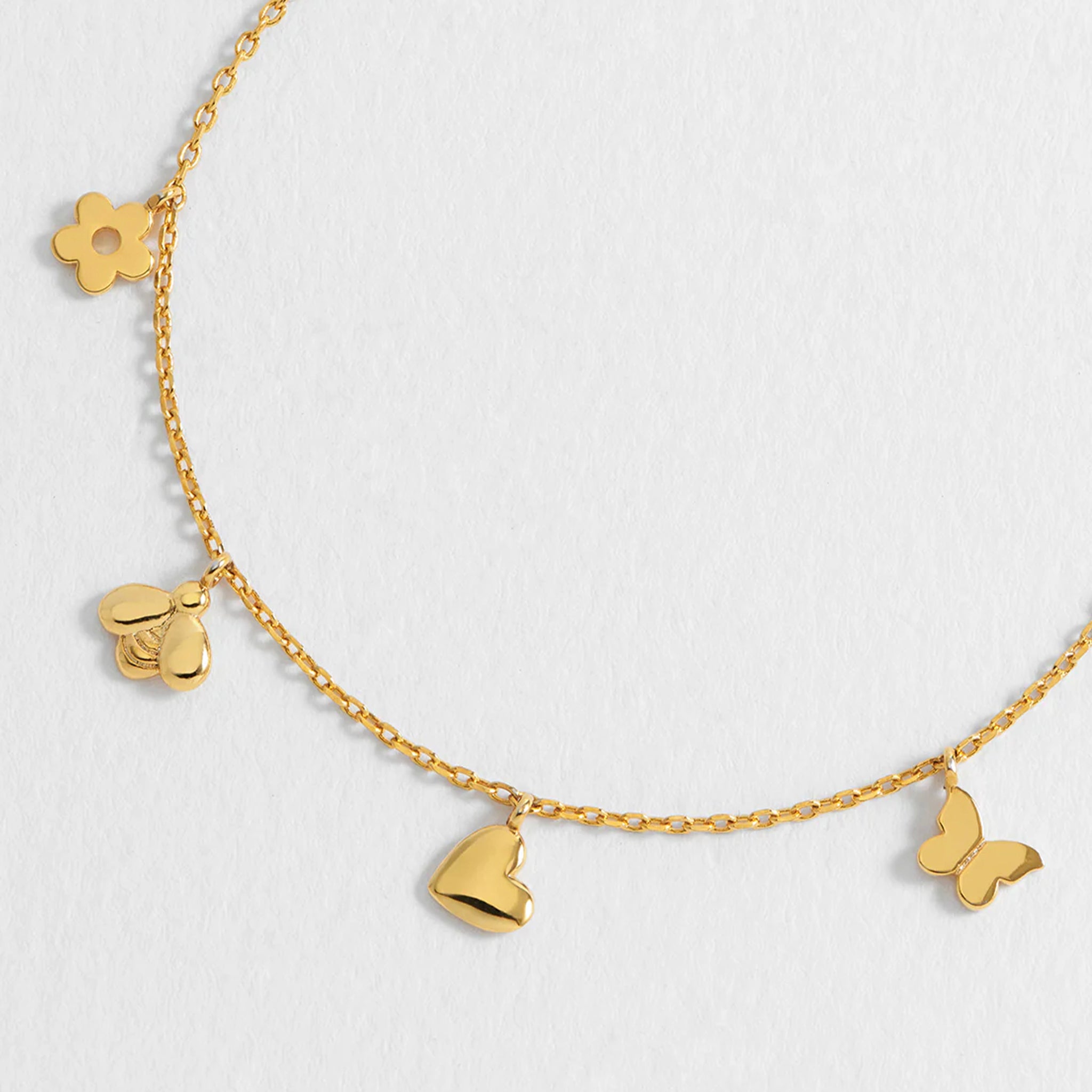 Gold necklace with various charms on a light gray background