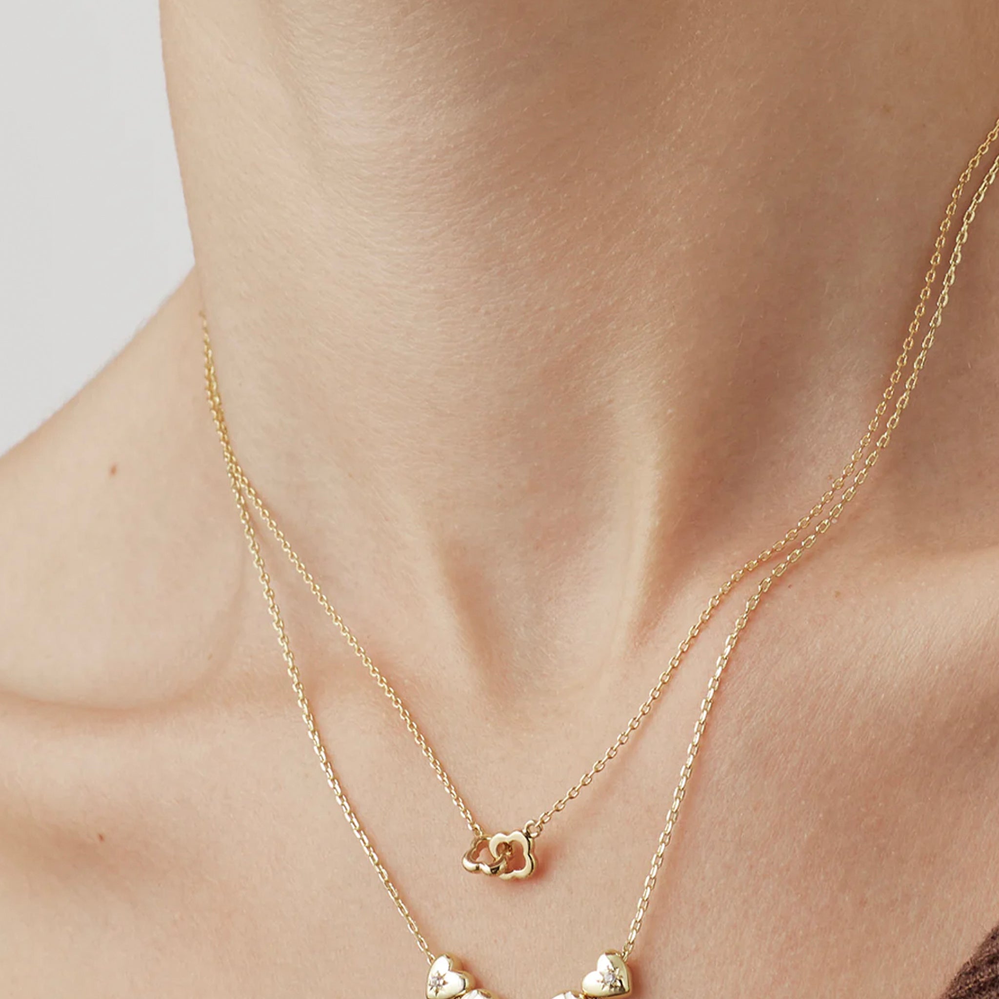 Gold necklace with a flower pendant on a person's neck against a neutral background