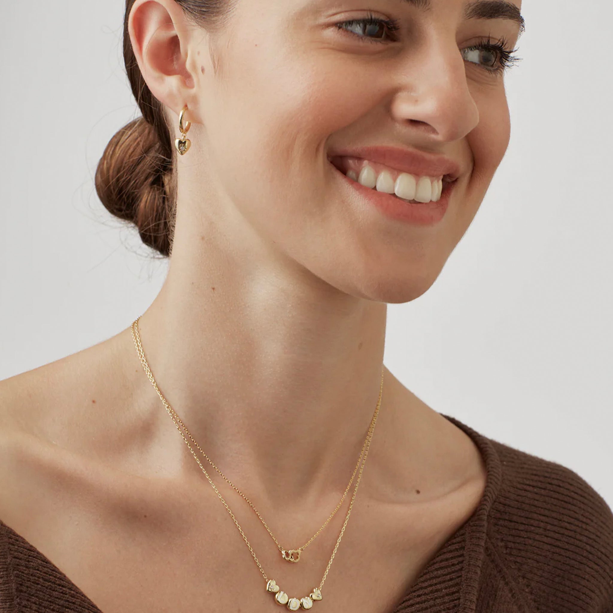 Woman wearing a gold necklace and earrings on a plain background