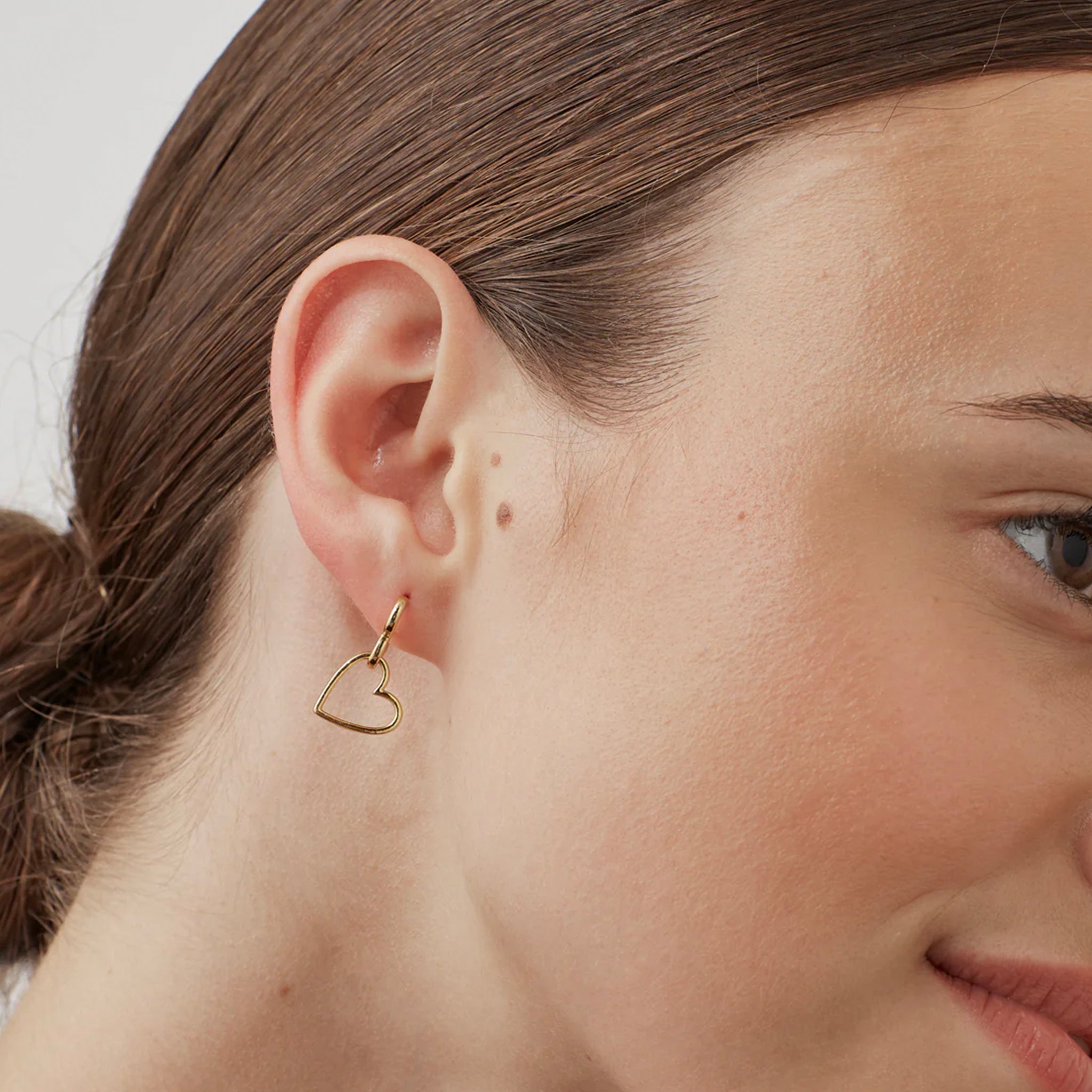 Close-up of a person wearing a gold heart-shaped earring.
