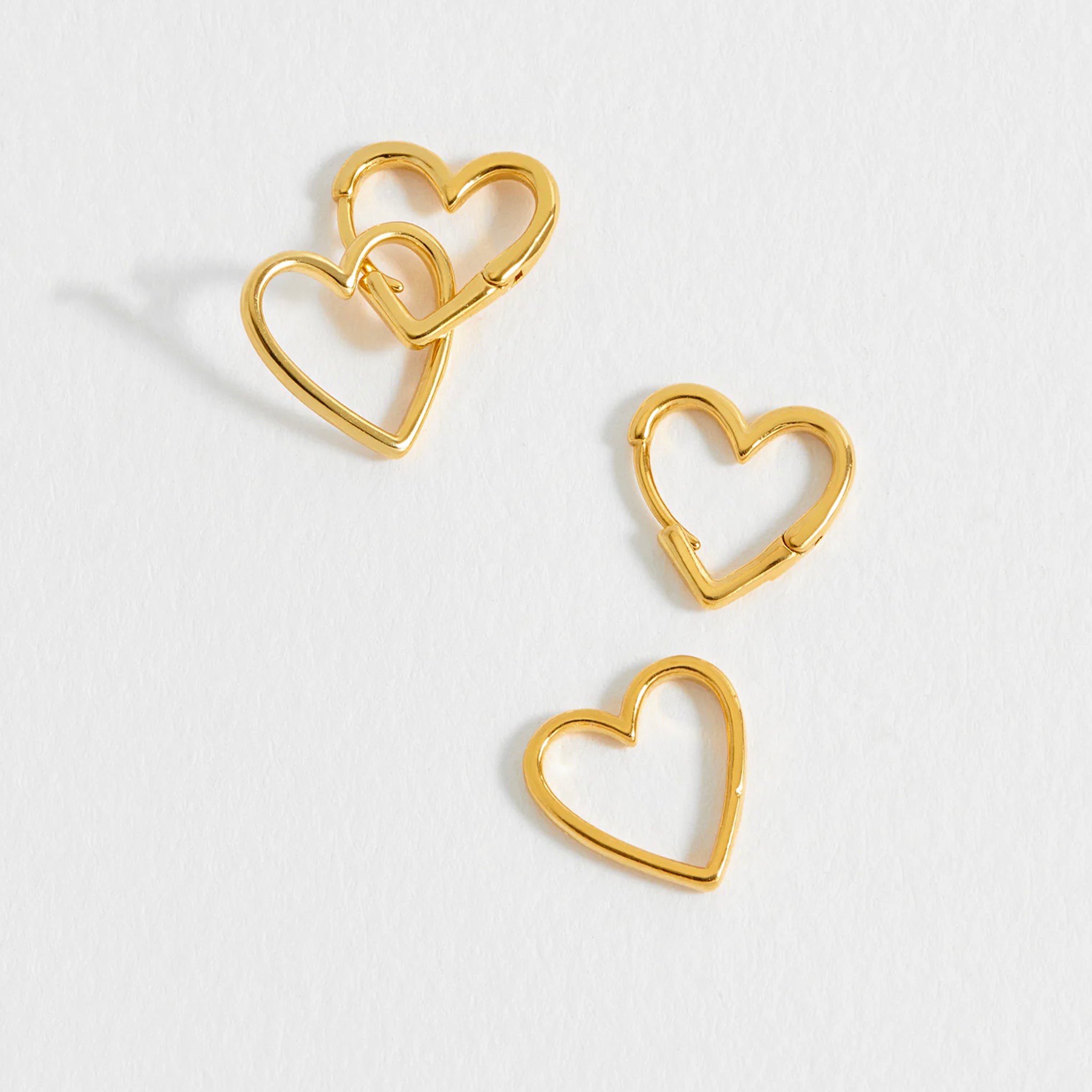 Gold heart-shaped earrings on a light gray background