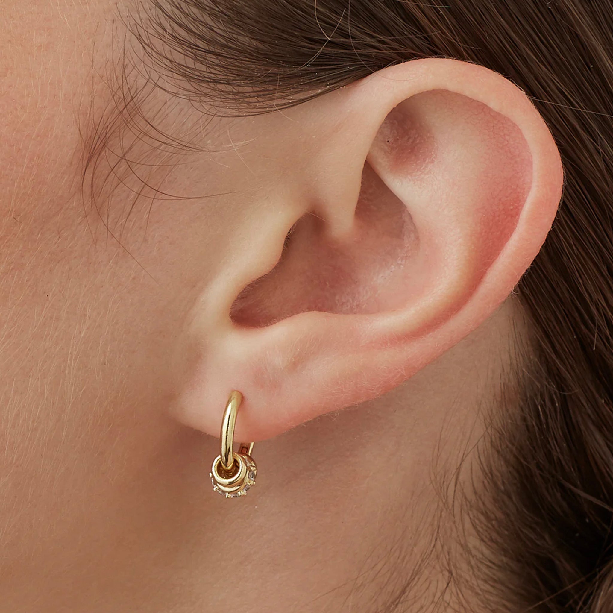 Close-up of an ear wearing a gold hoop earring with a small round charm.