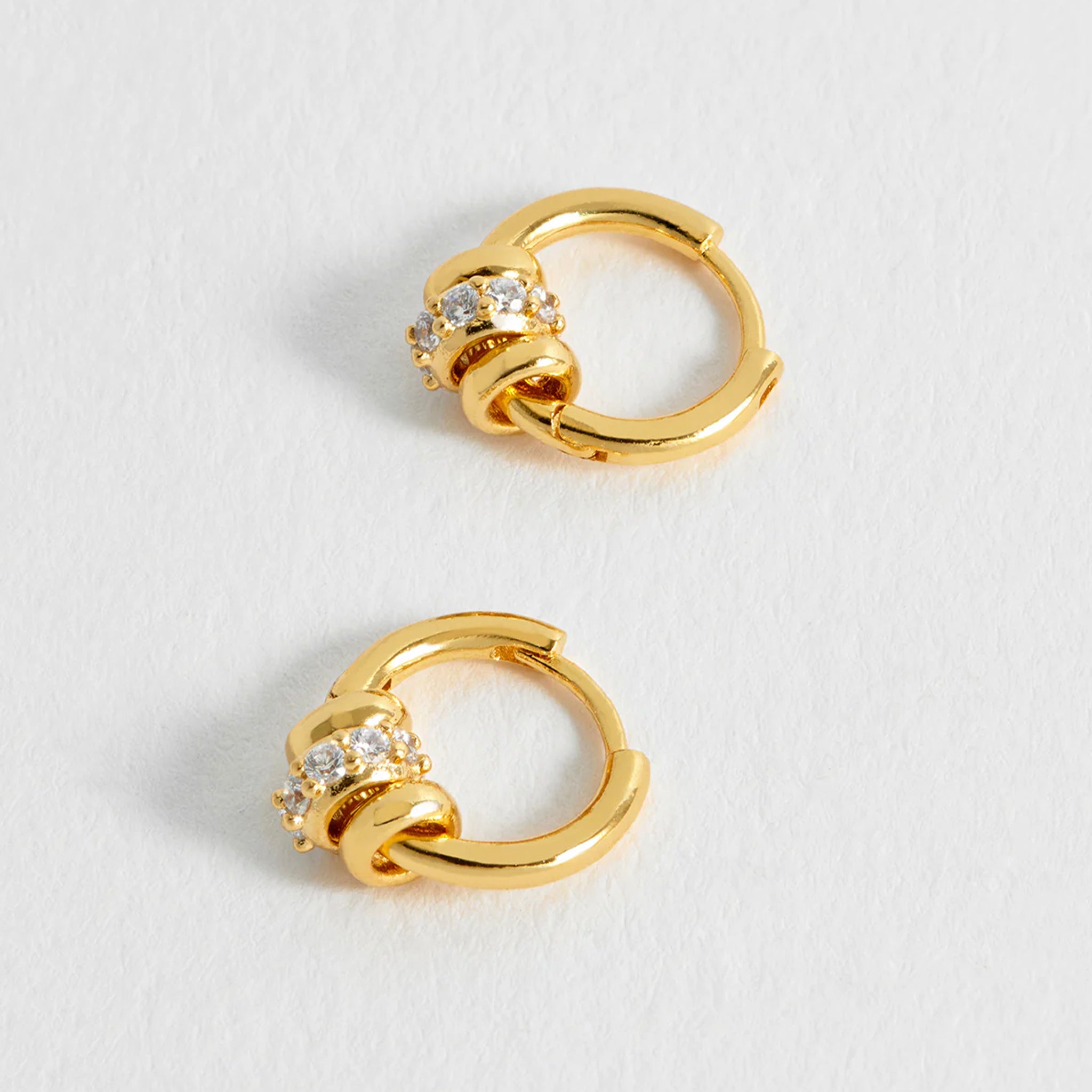 Pair of gold hoop earrings with small diamonds on a light gray background