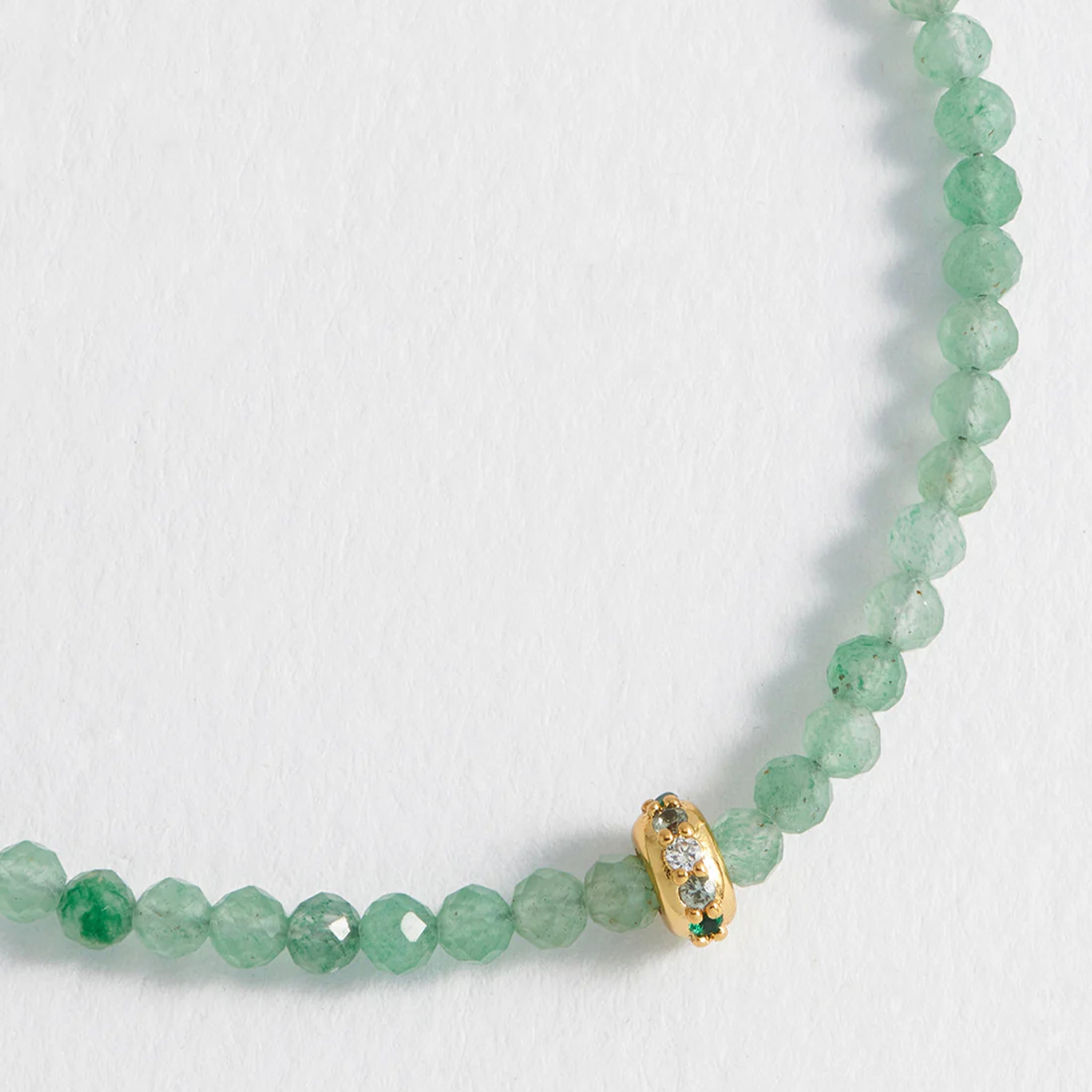 Green beaded bracelet with a gold and green charm on a white background