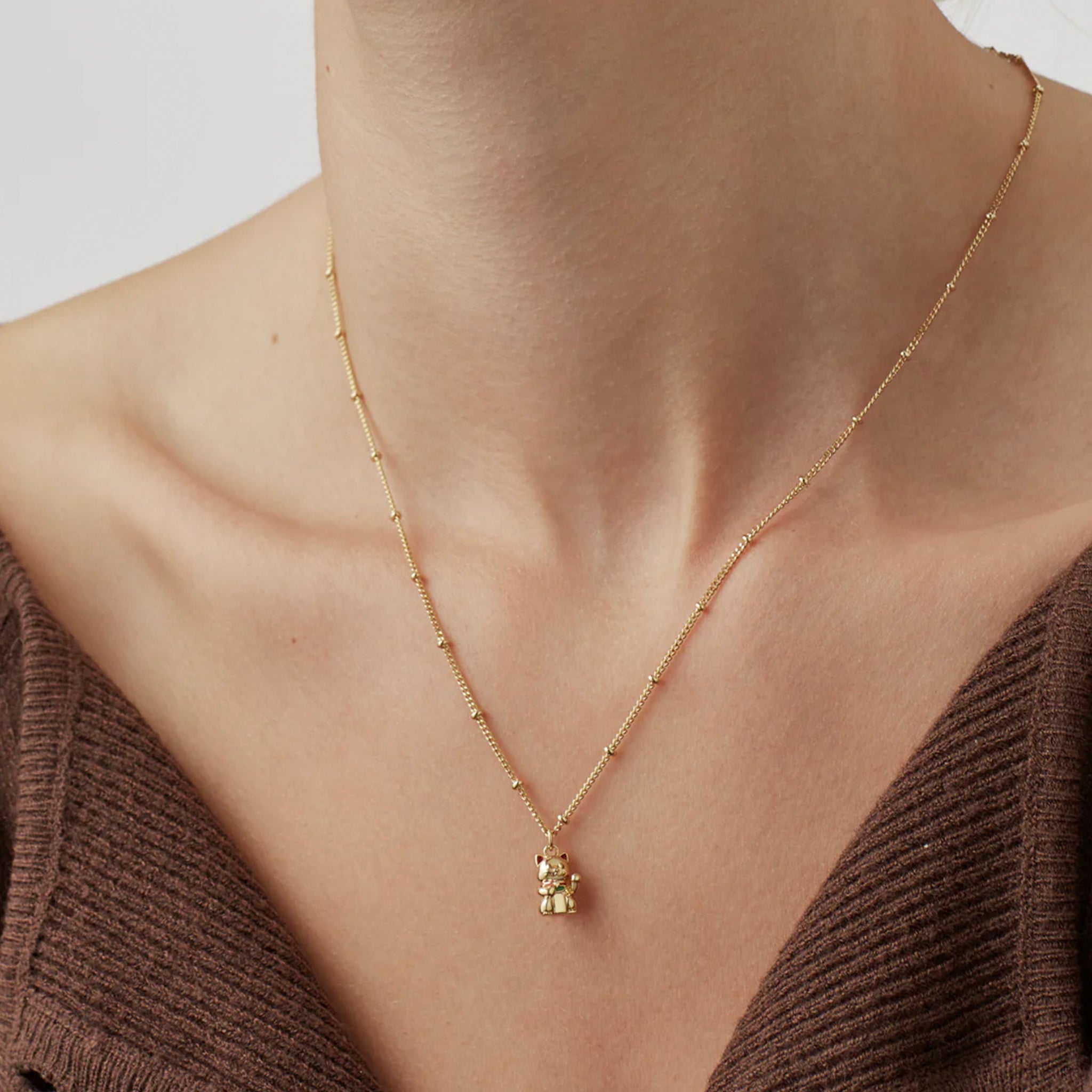 Gold necklace with a small pendant worn by a person in a brown sweater.