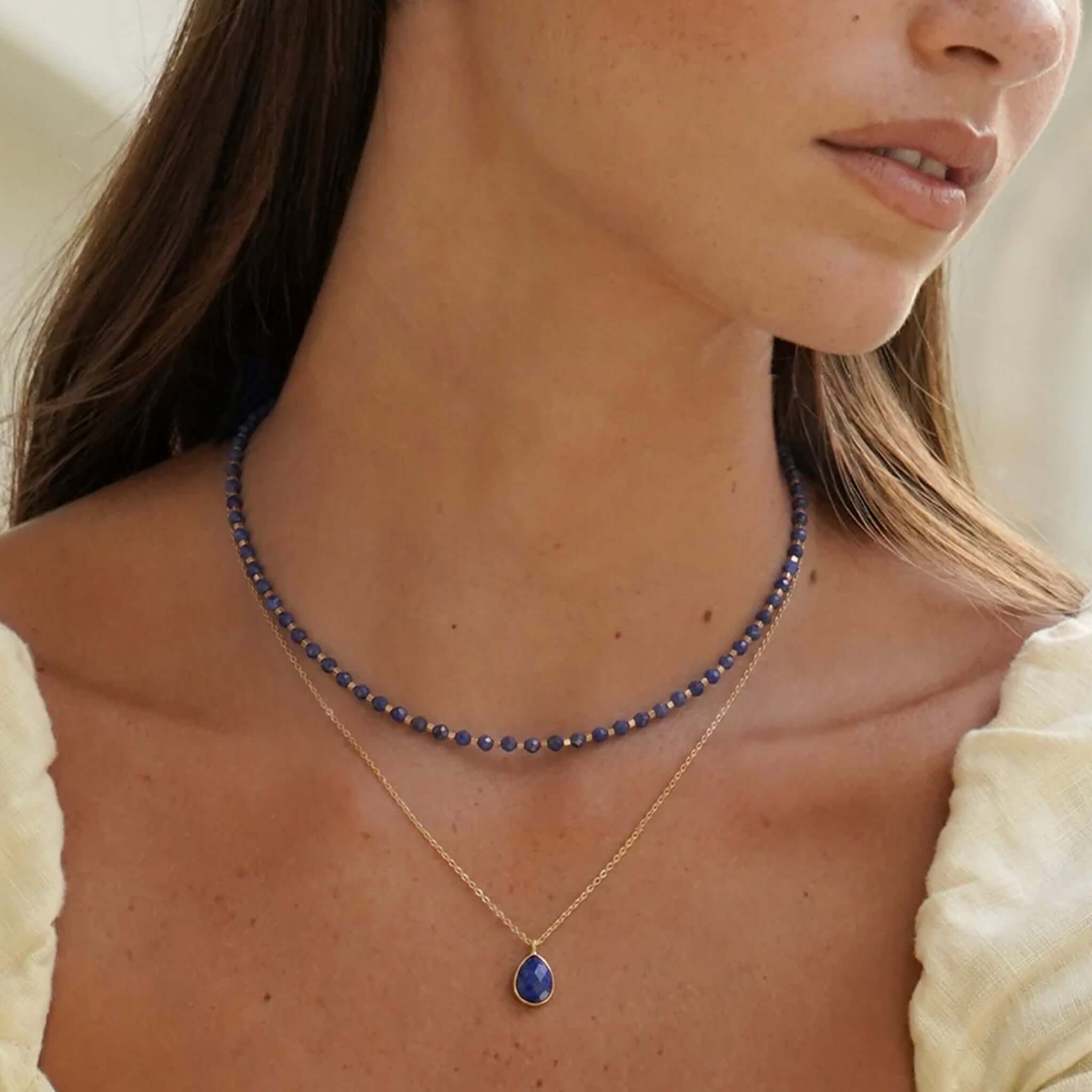 Estella Bartlett Wellness Faceted Teardrop Necklace - Sodalite worn with a beaded necklace, showcasing its rich navy color and design.
