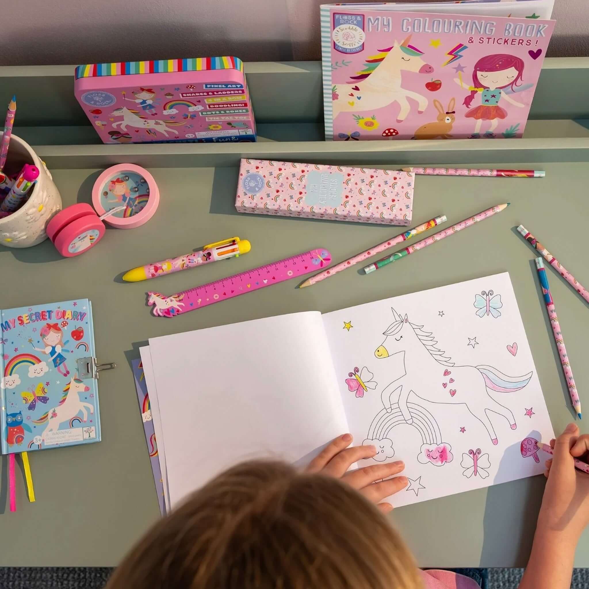 Alt Tag: Floss & Rock My Colouring Book Scribble Sniff - Rainbow Fairy kids colouring book with unicorn page, pencils and stickers on desk