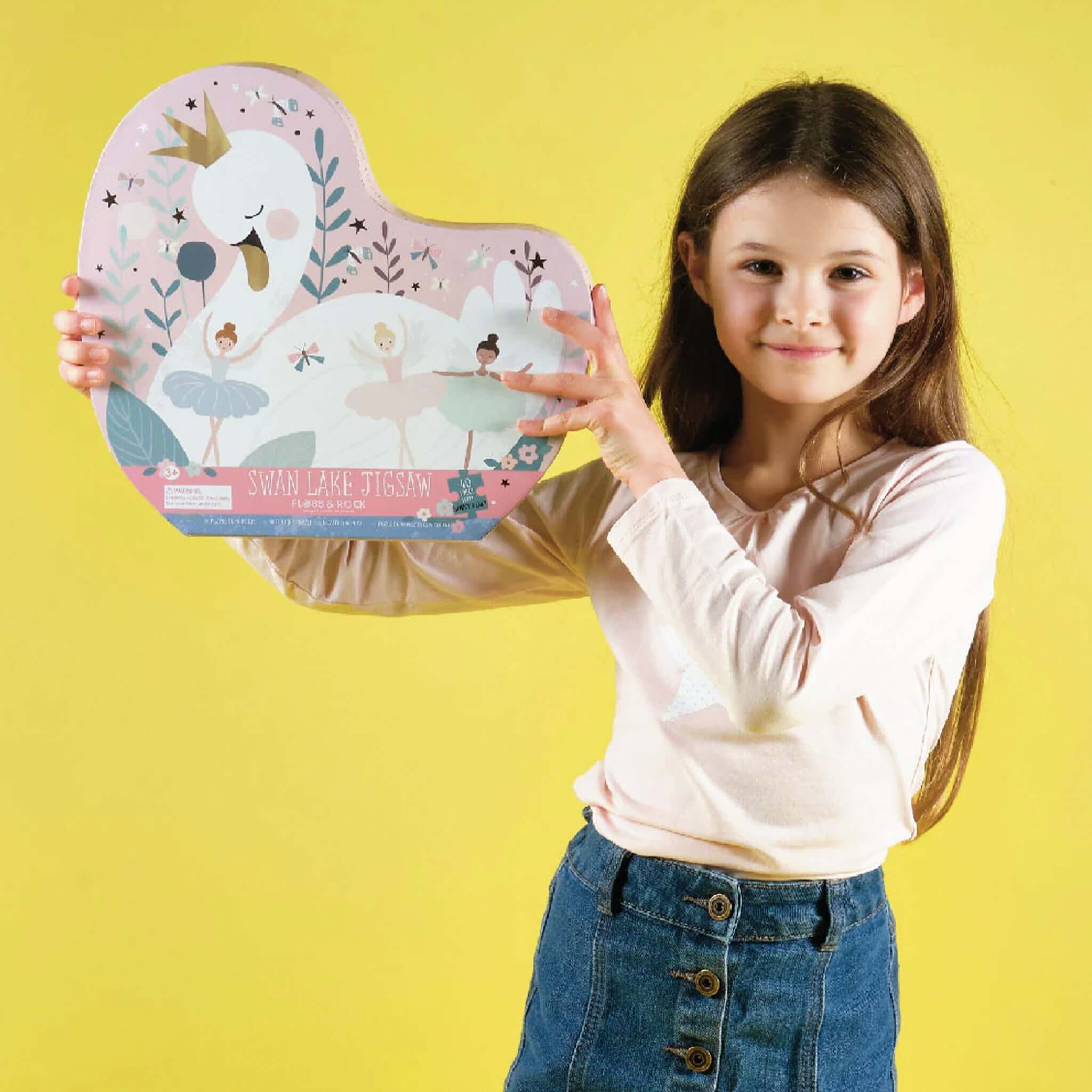 Child holding Floss & Rock Swan Shaped Jigsaw Puzzle - Enchanted box against a yellow background.