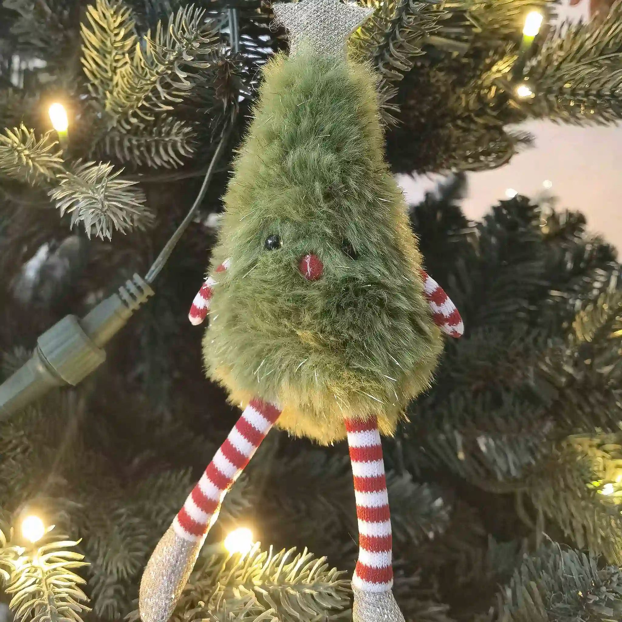 Green plush creature with red and white striped legs hanging on a Christmas tree.