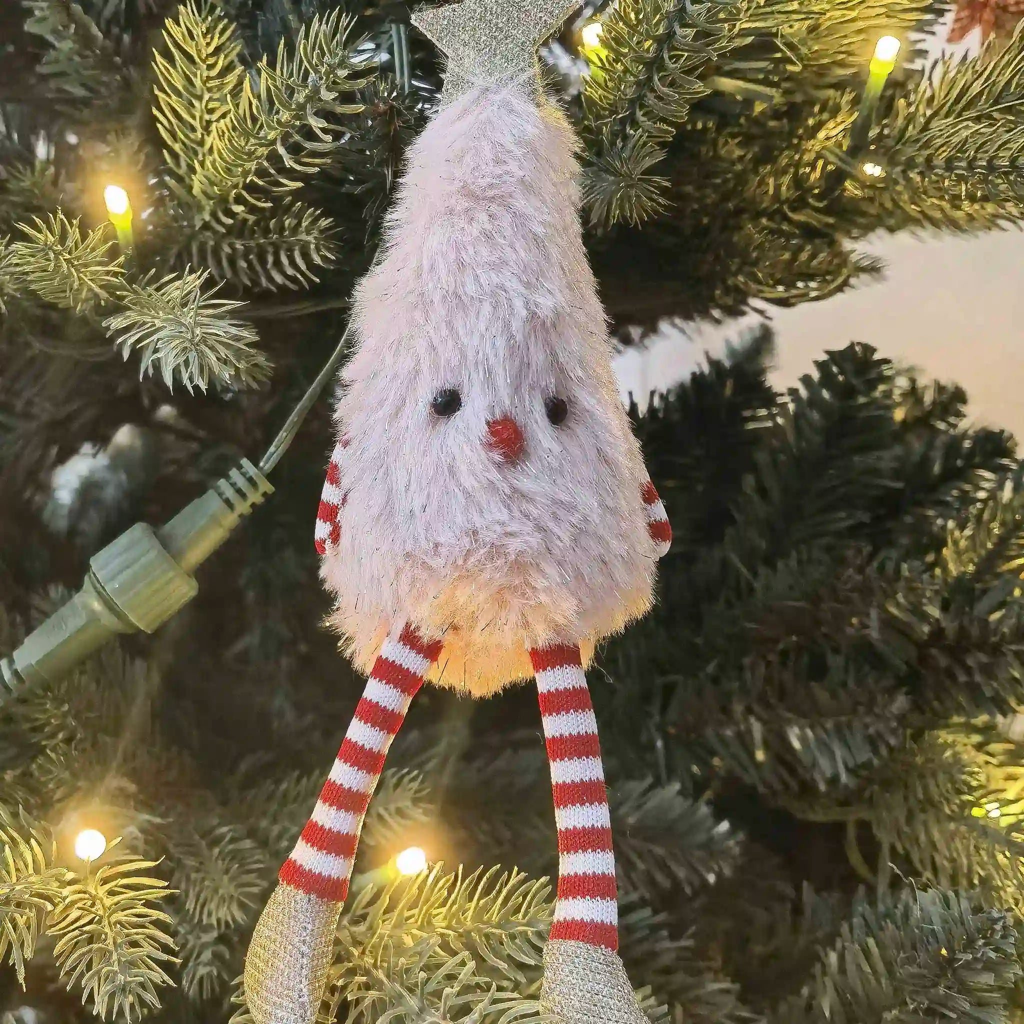 Fluffy Christmas tree ornament with striped legs hanging on a decorated tree.