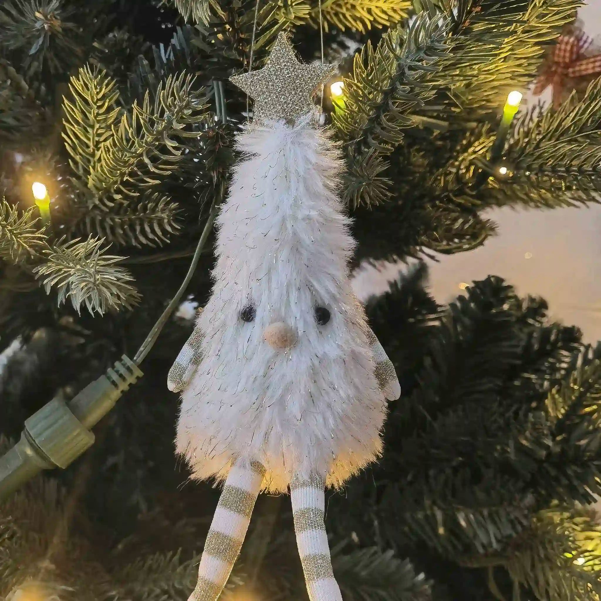 White decorative figure with gold accents hanging on a Christmas tree.