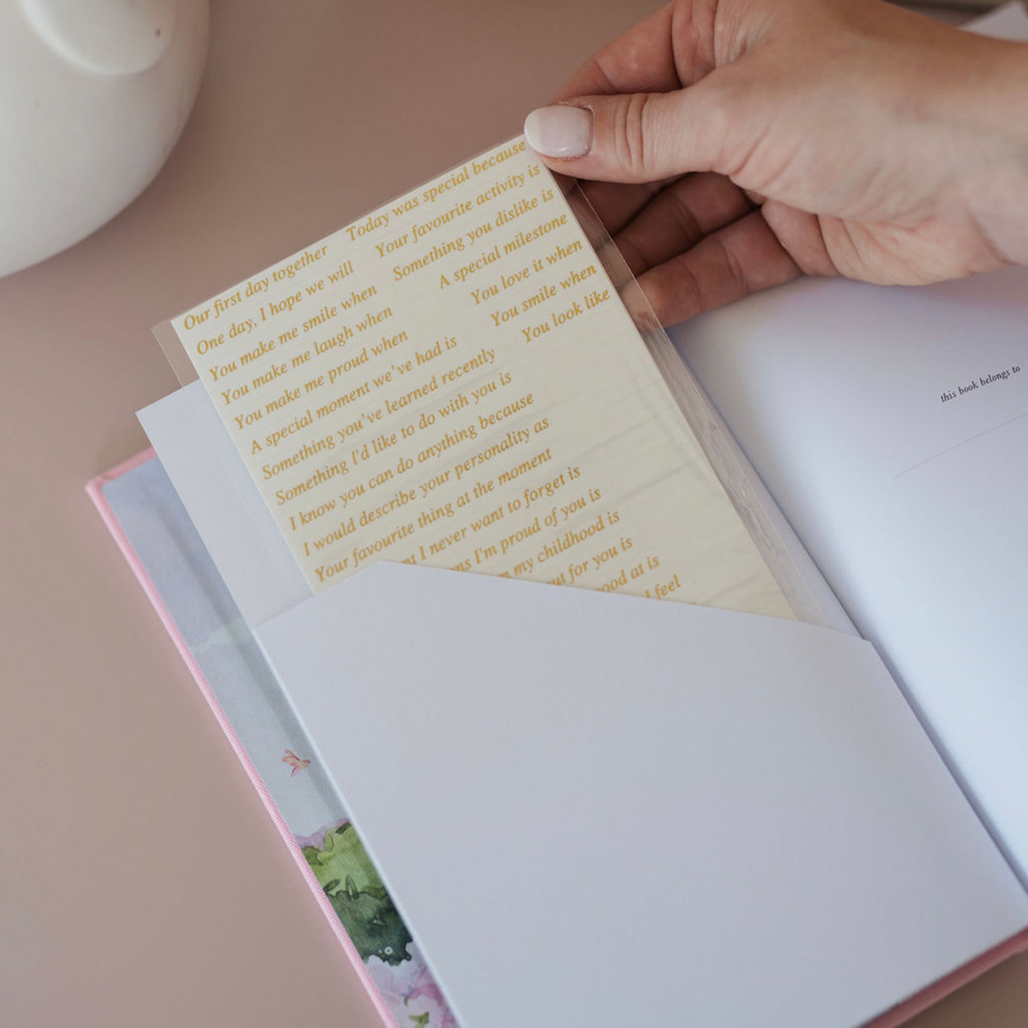 Hand holding a letter with gold text inside an open book on a light surface.