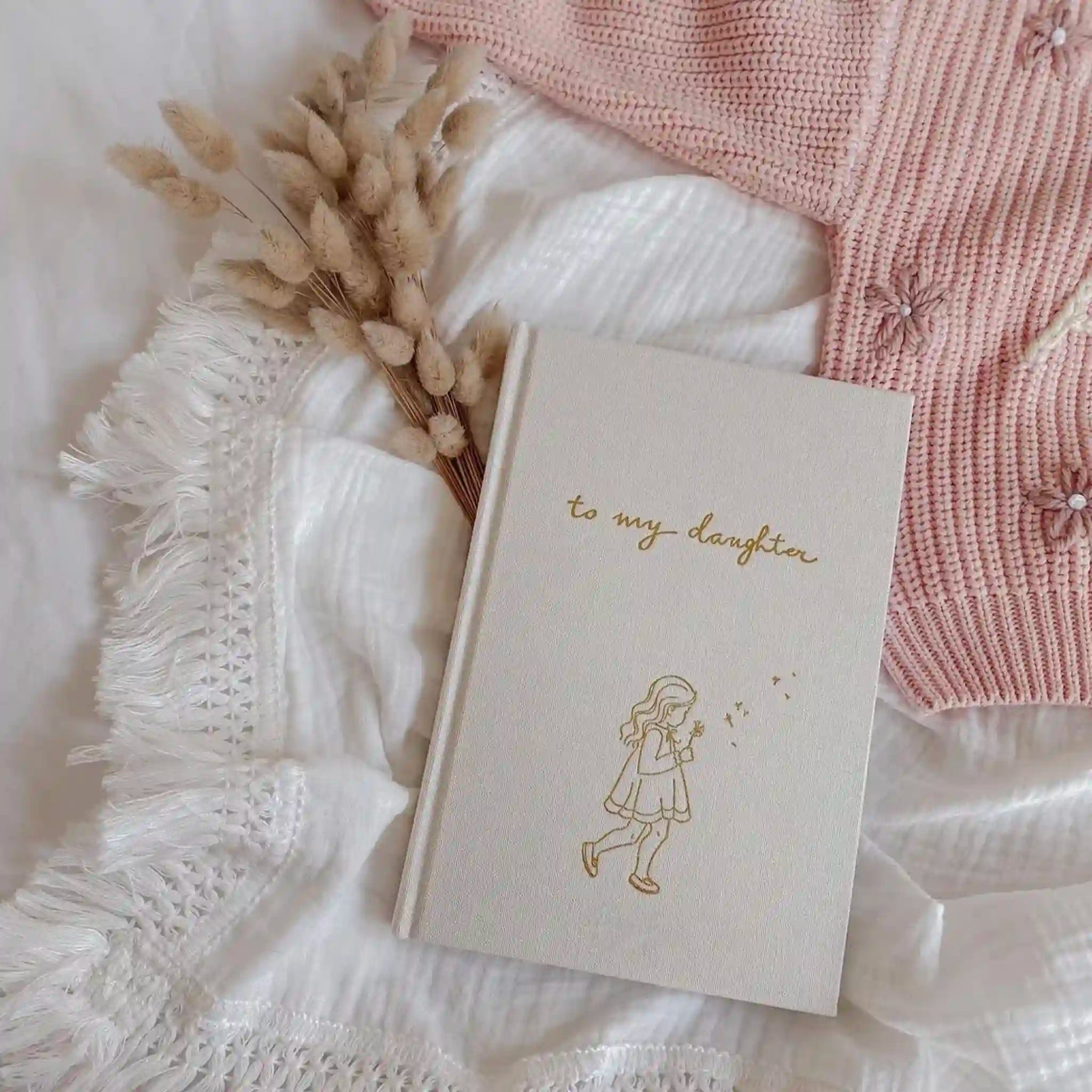 Notebook with 'to my daughter' text and a girl illustration on a soft surface with a pink textured blanket.