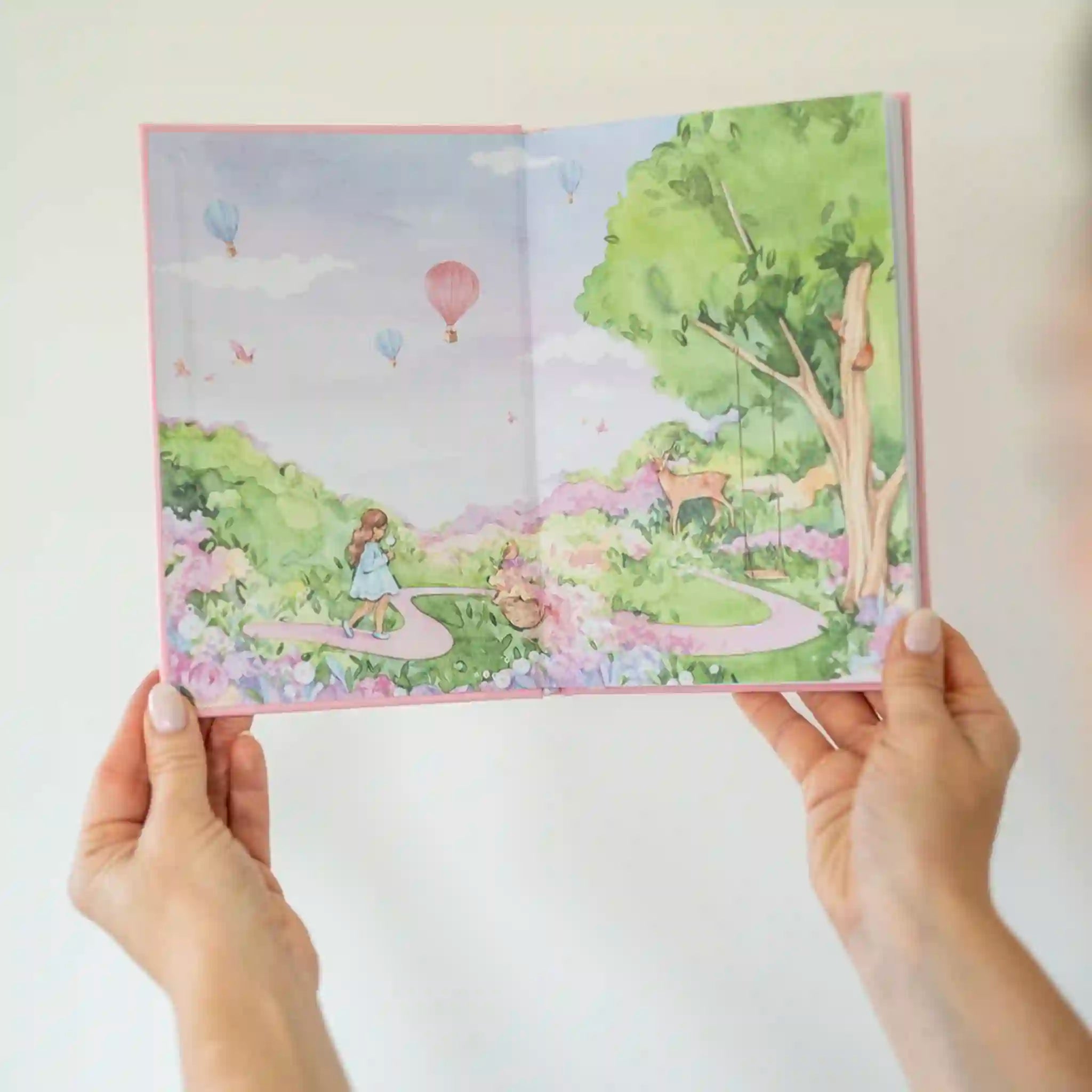 Illustrated book open to a colorful scene with trees, flowers, and hot air balloons.