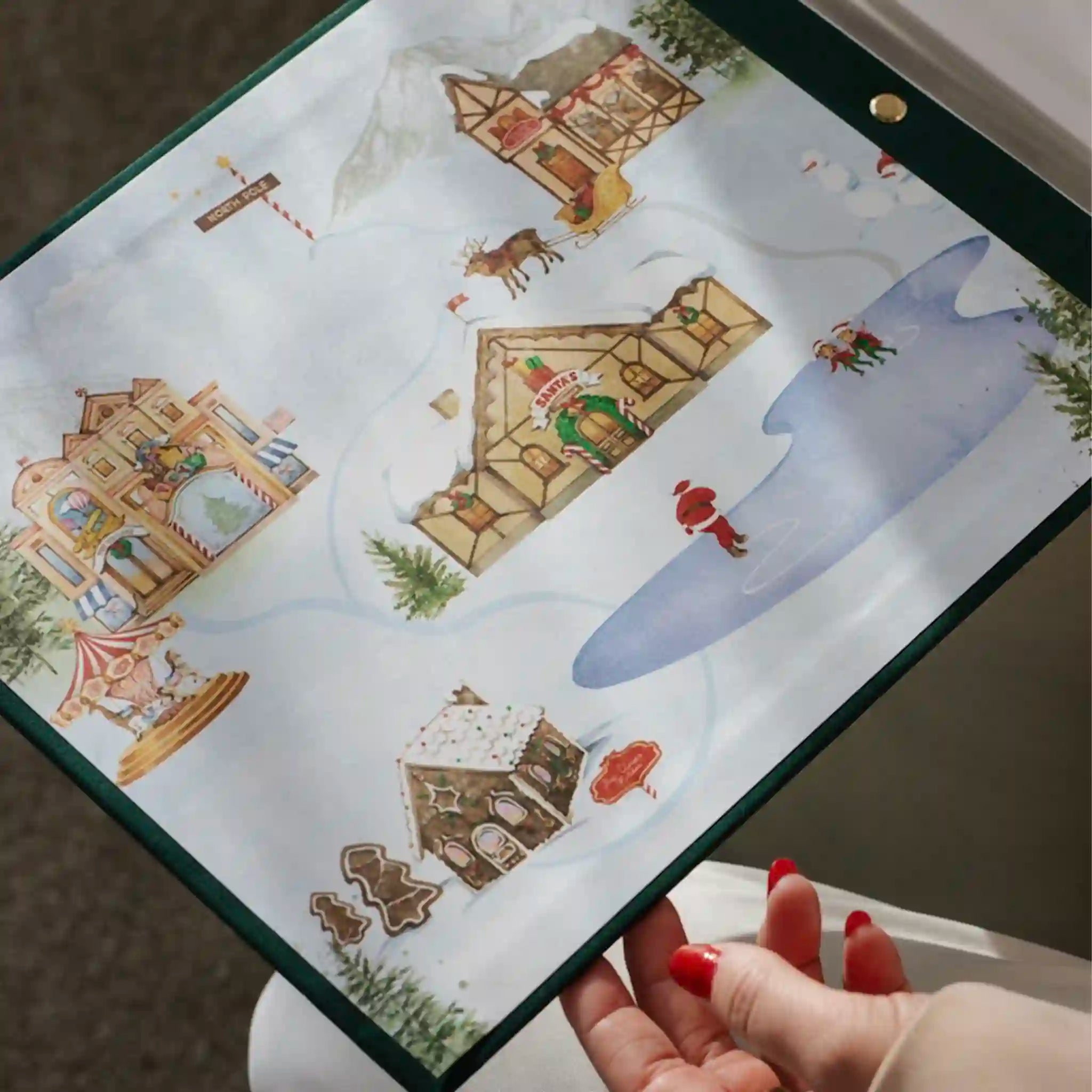 Hand holding a Christmas-themed advent calendar with gingerbread houses and Santa Claus.