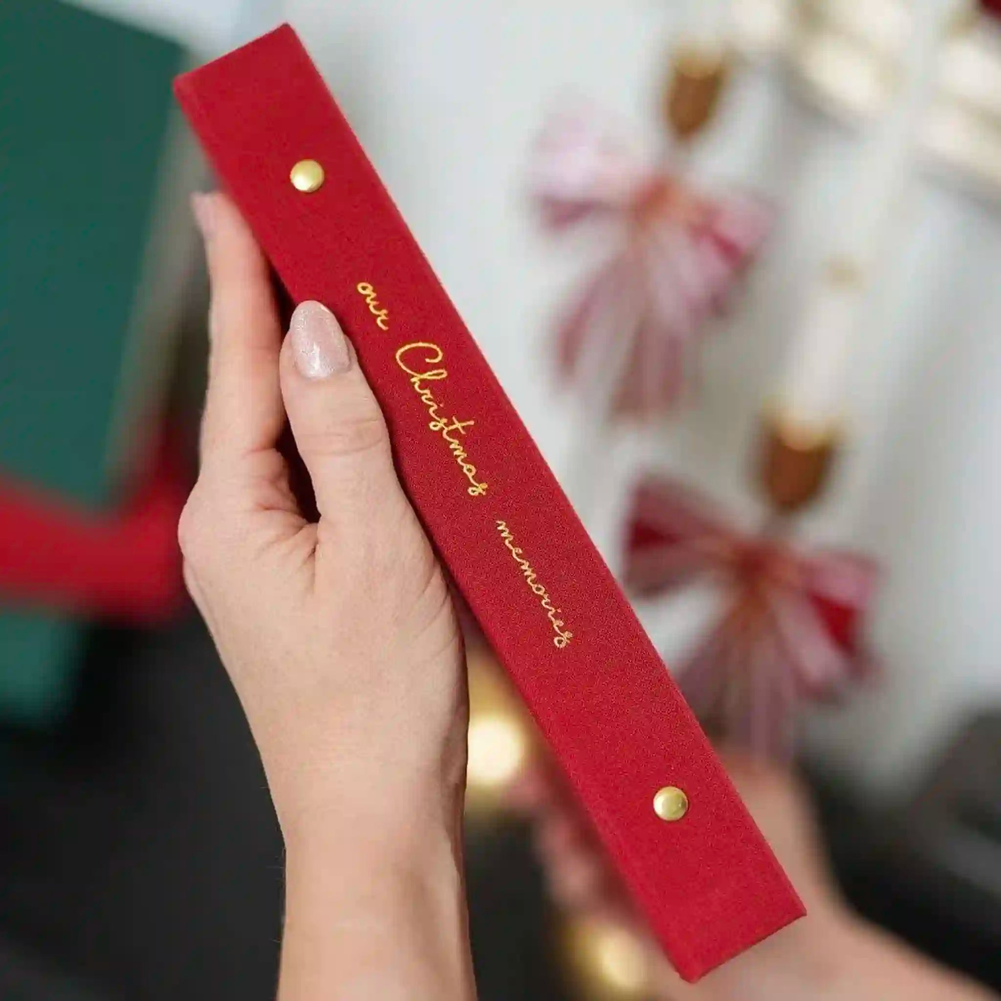 Red box with gold text held by a hand, Christmas decorations in the background
