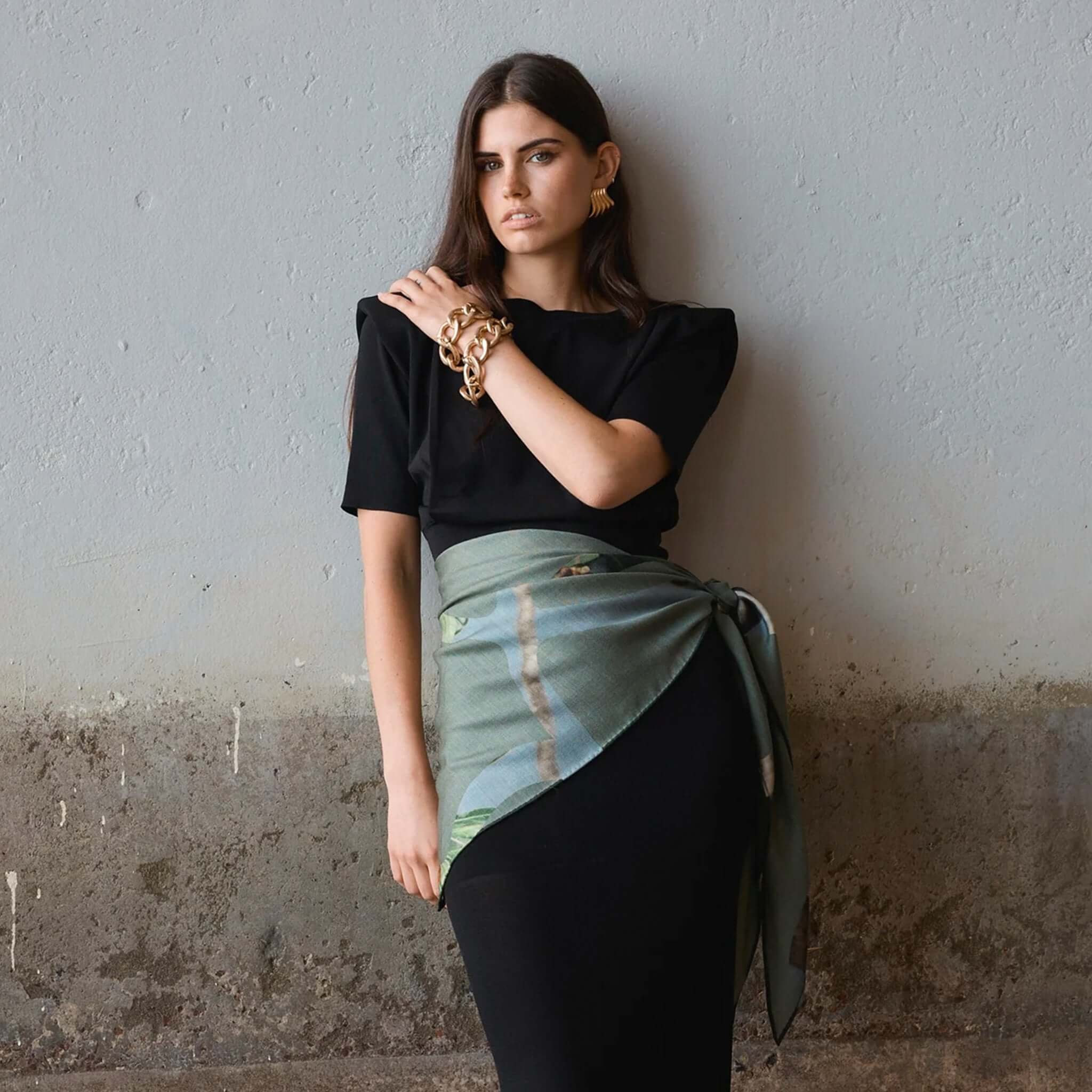 Alt Tag: Good & Co Heritage Triangle Wool & Silk Scarf - Olive worn as an olive triangle wrap with heritage logo print, wool-silk herringbone