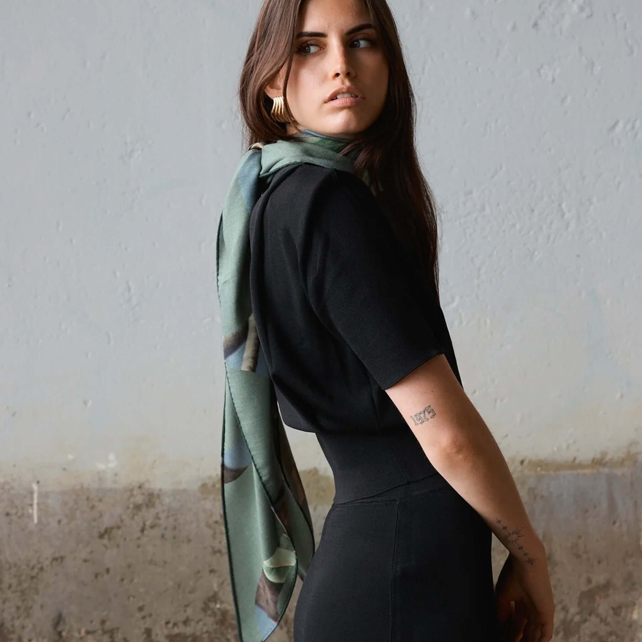 Alt Tag: Good & Co Heritage Triangle Wool & Silk Scarf - Olive worn by model, oversized olive triangle scarf with heritage logo print