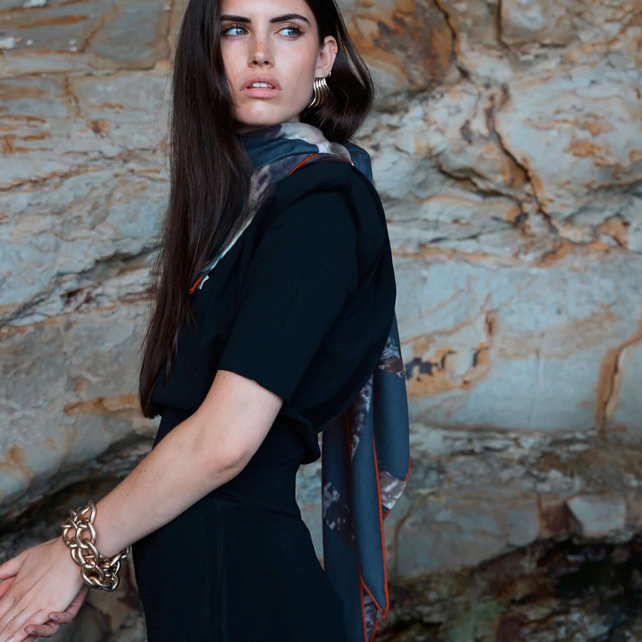 Alt Tag: Good & Co Heritage Triangle Wool & Silk Scarf - Petrol worn by model, oversized triangle wool-silk herringbone scarf with heritage logo print