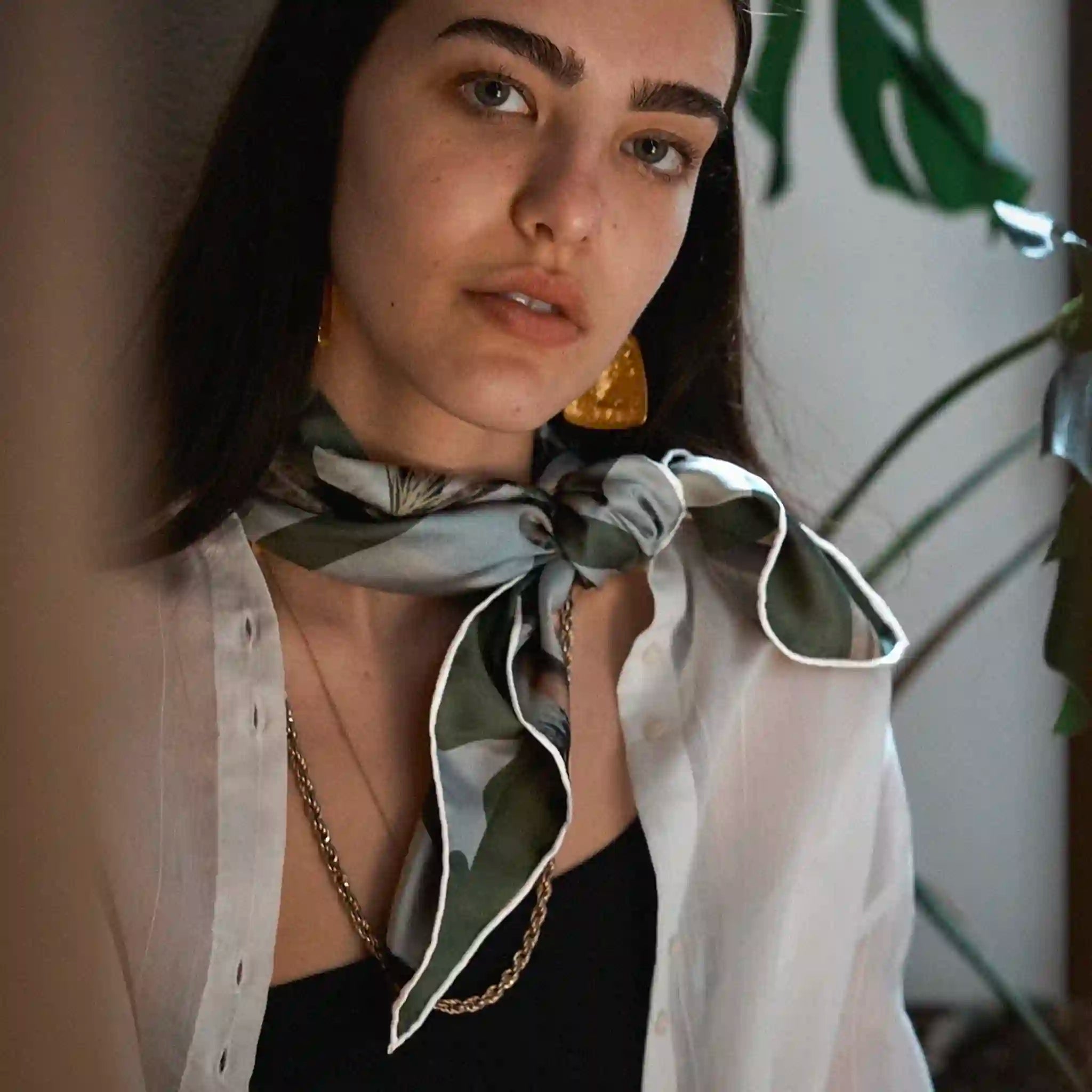 Woman wearing a white blouse with a green patterned scarf around her neck, indoors.