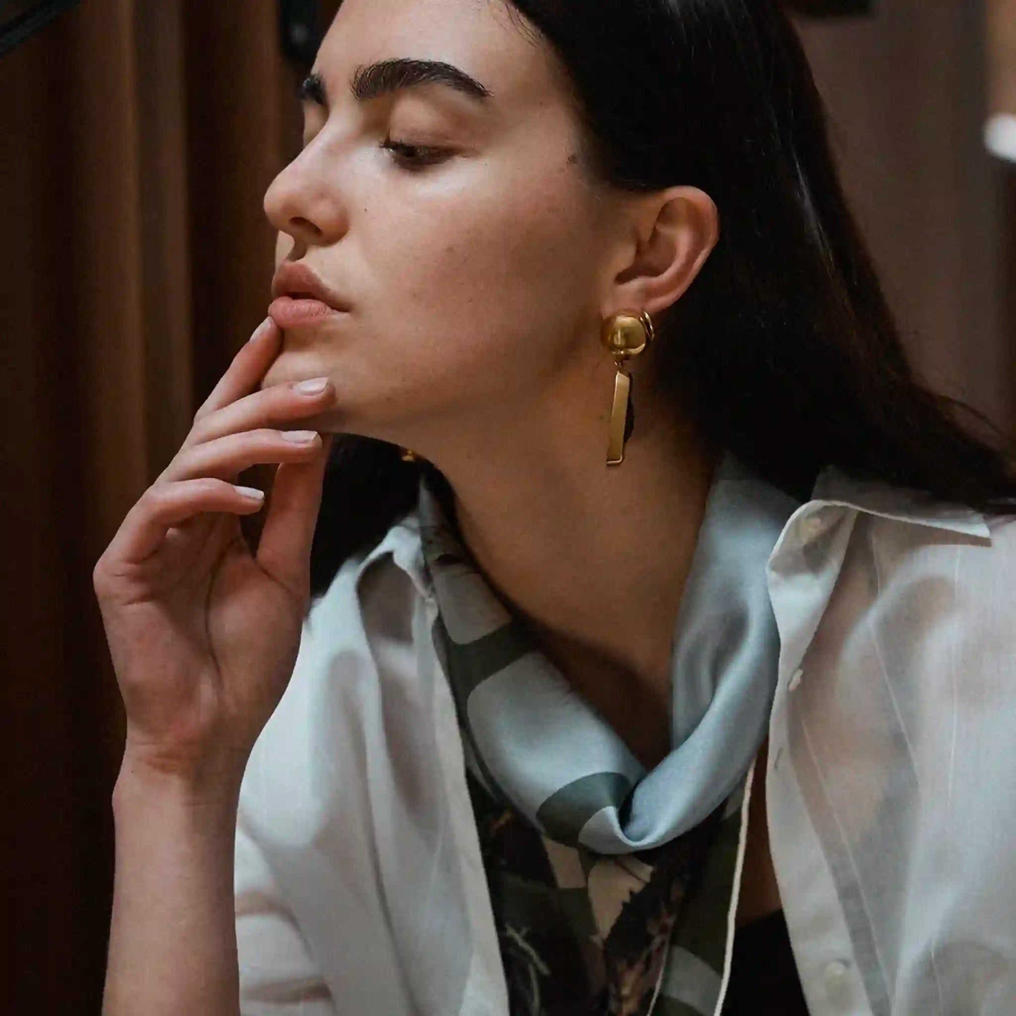 Woman wearing gold earrings and a patterned scarf with a blurred background