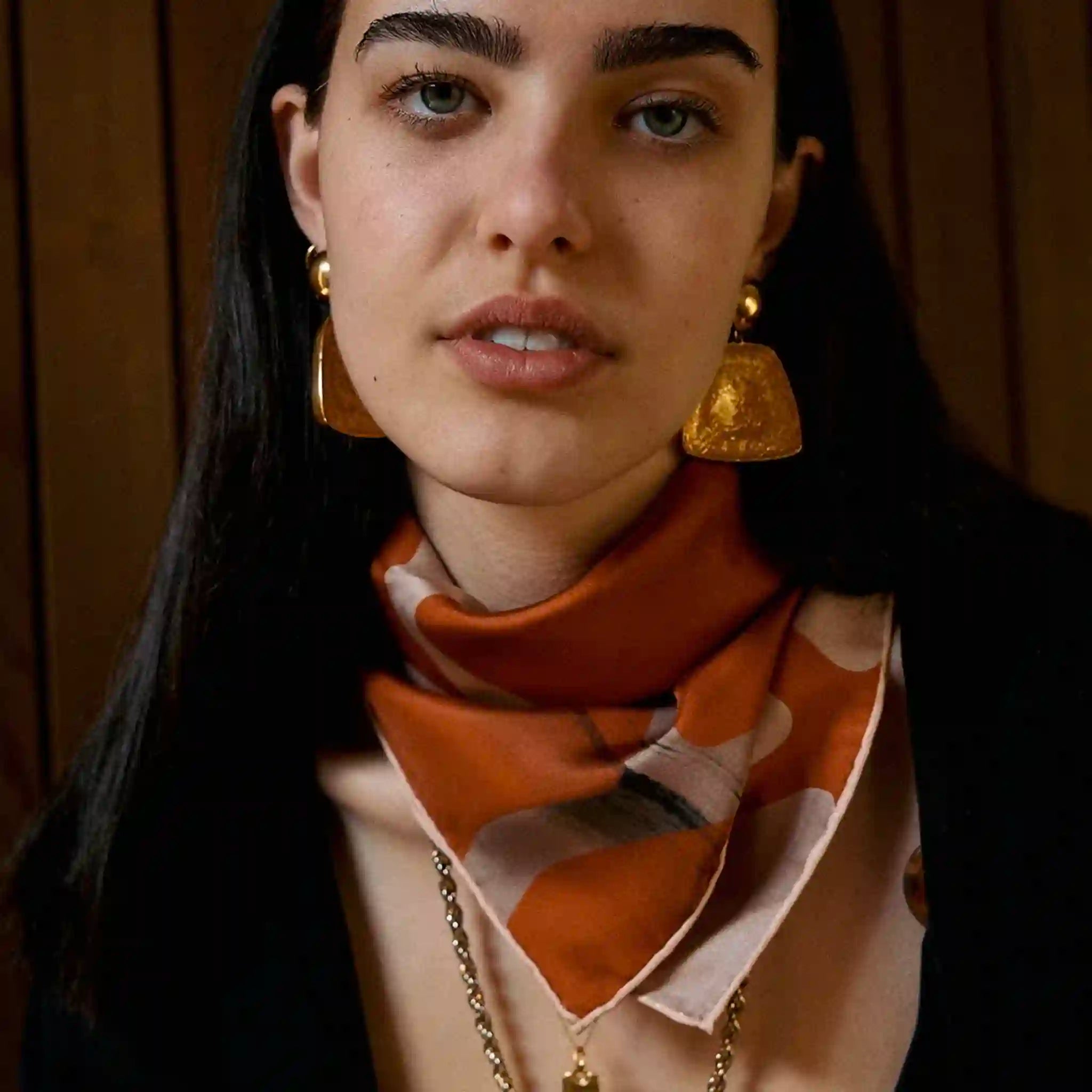 Woman wearing a patterned scarf and gold earrings with a wooden panel background