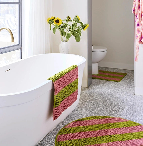 Bathroom with a white bathtub, toilet, and green and pink striped bath mats.