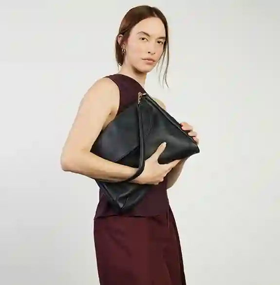Person holding a black clutch bag against a plain background