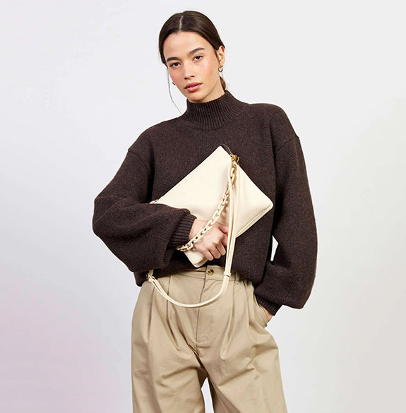 Woman holding a beige clutch bag against a plain background