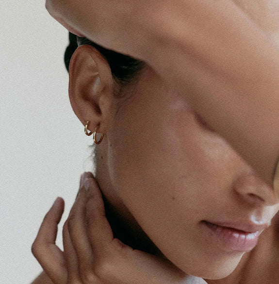 Close-up of a person wearing gold hoop earrings with a neutral background