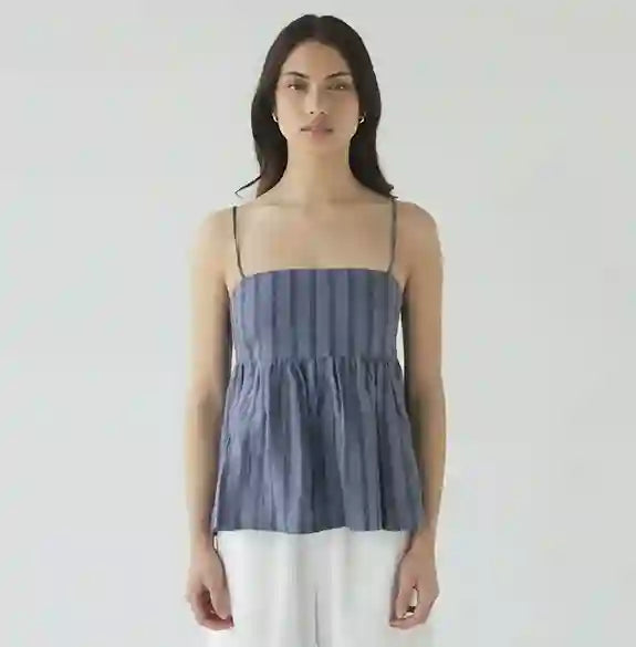 Woman wearing a blue striped top and white pants against a plain background