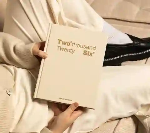 Person holding a beige notebook with 'Two thousand Twenty Six' printed on it.