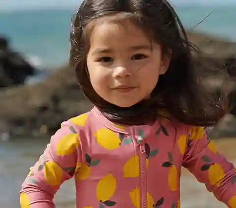 Child wearing a pink and yellow swimsuit with pineapple pattern on a beach.