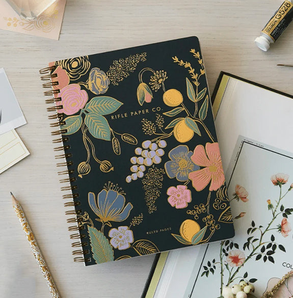 Floral notebook with 'Rifle Paper Co' branding on a light wooden surface.
