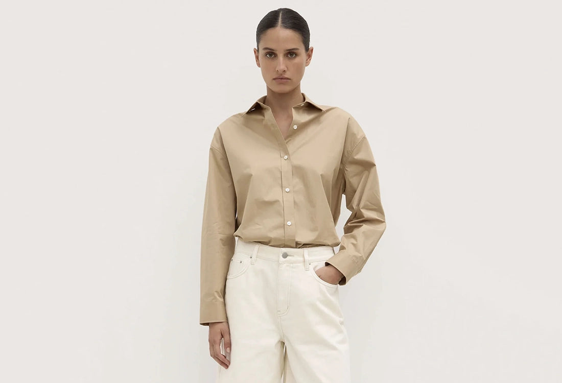 Woman wearing a beige shirt and white pants against a plain background