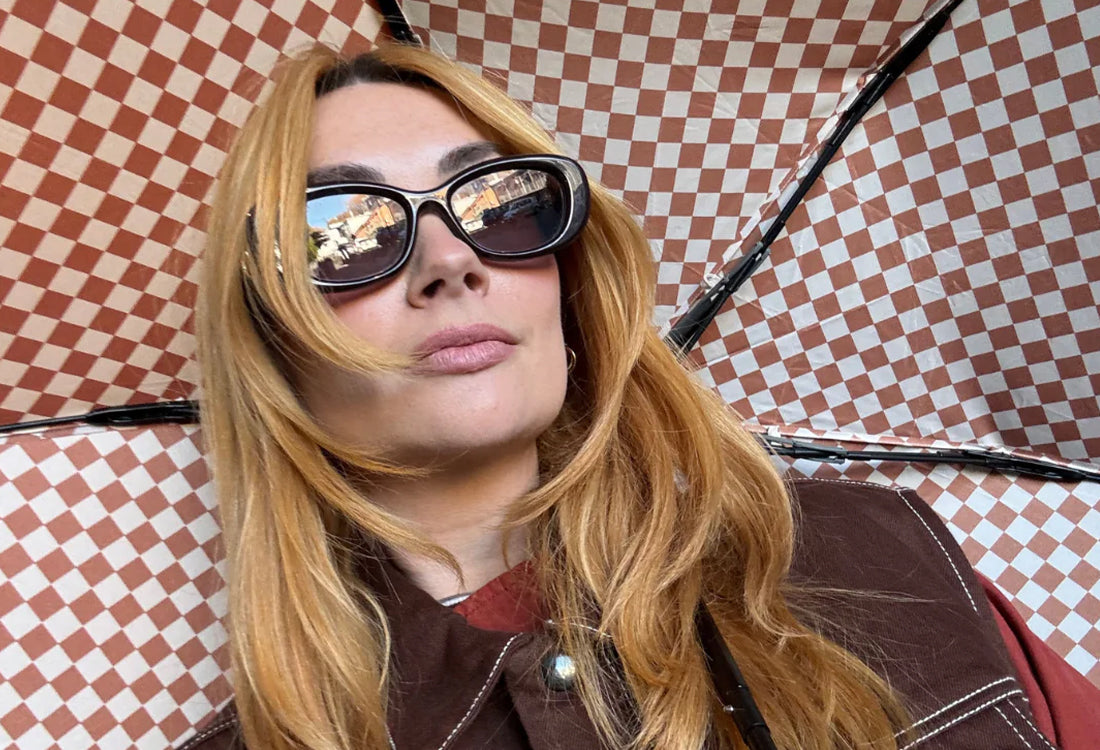 Woman wearing sunglasses and a brown jacket against a checkered background