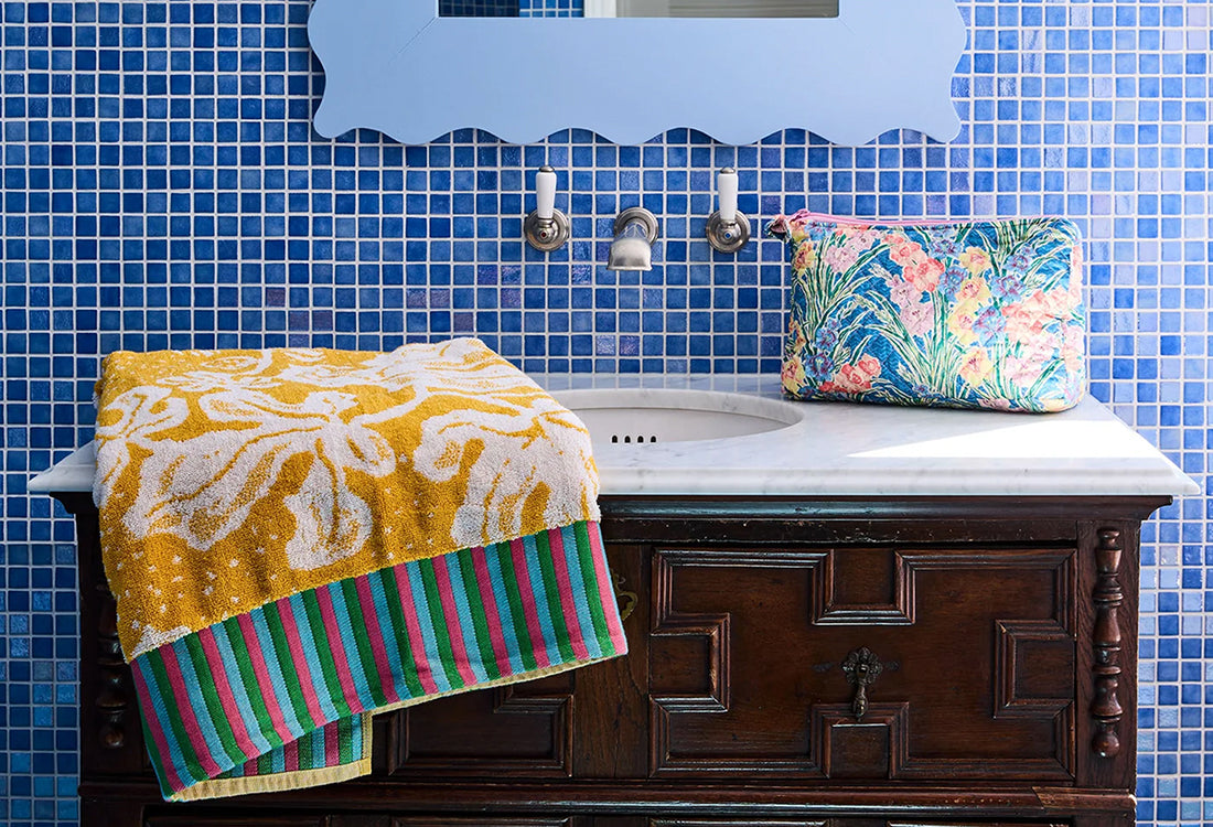 Bathroom with blue tiled walls, wooden vanity, and colorful towels.