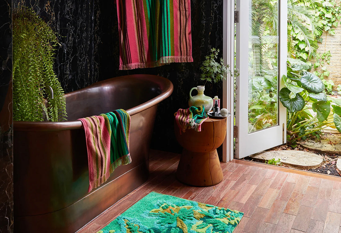 Bathroom with a freestanding bathtub, colorful towels, and a view of greenery outside.