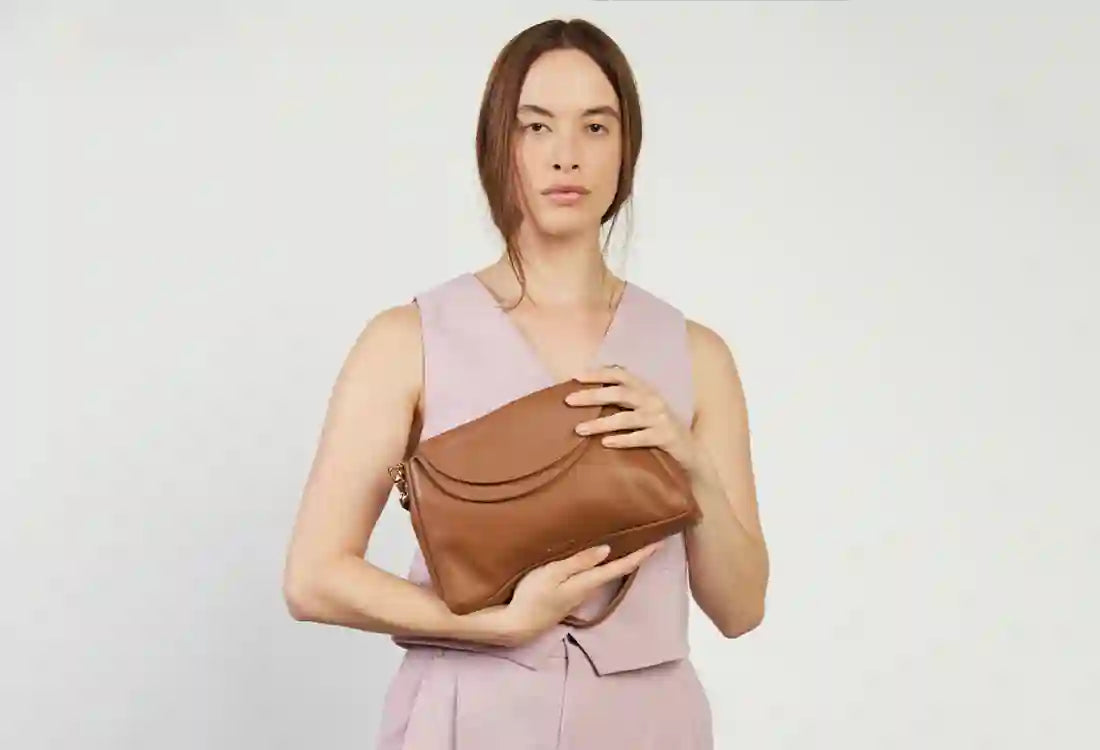 Woman holding a brown leather handbag against a plain background