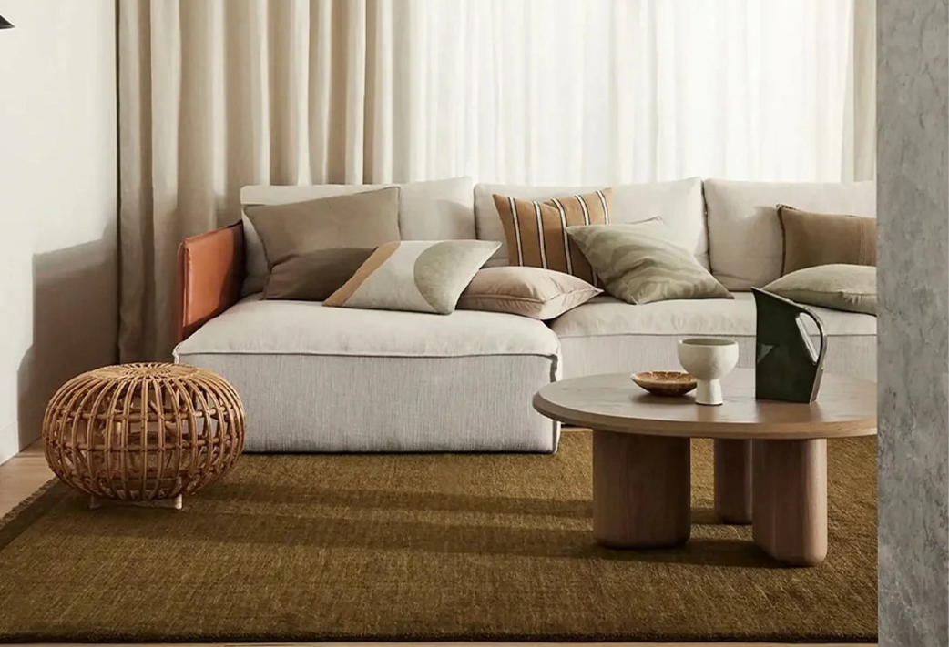 Modern living room with a beige sectional sofa, wooden coffee table, and decorative items.