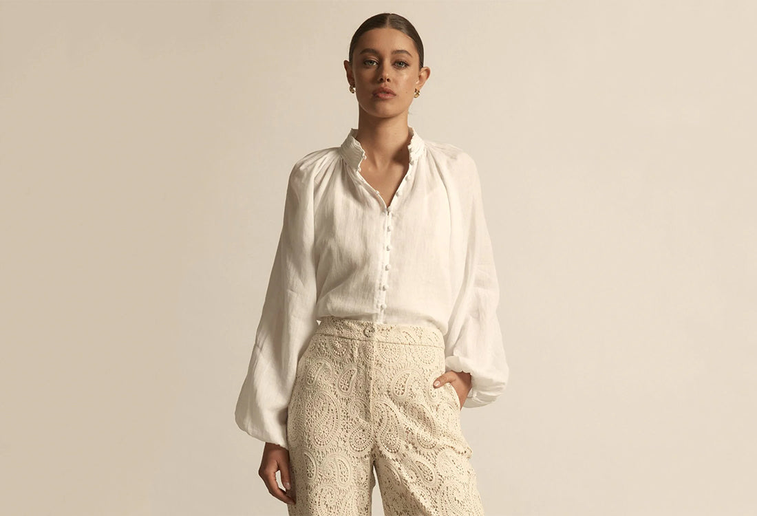 Woman wearing a white shirt and beige pants against a plain background