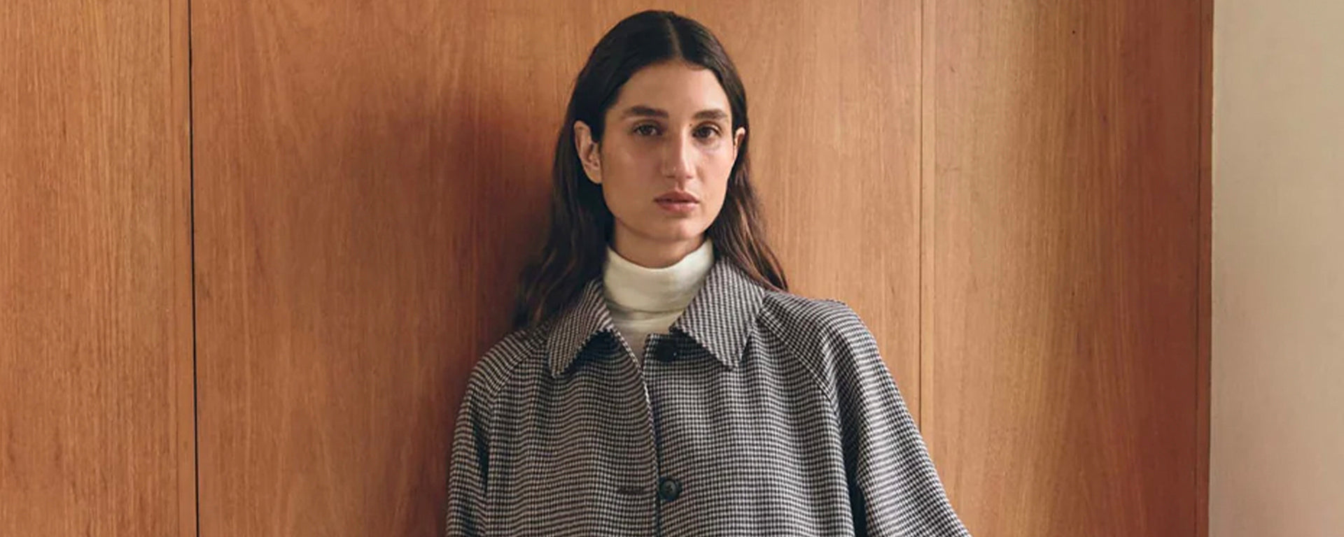 Woman wearing a checkered coat against a wooden wall
