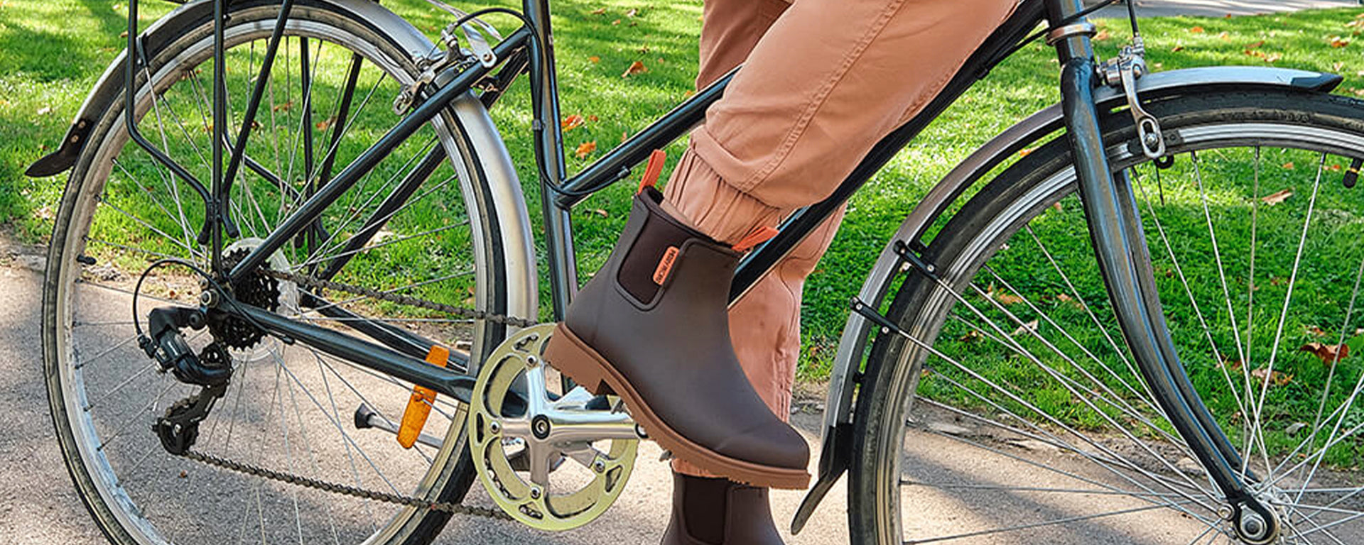 Person wearing brown rain boots standing next to a bicycle on a grassy area.