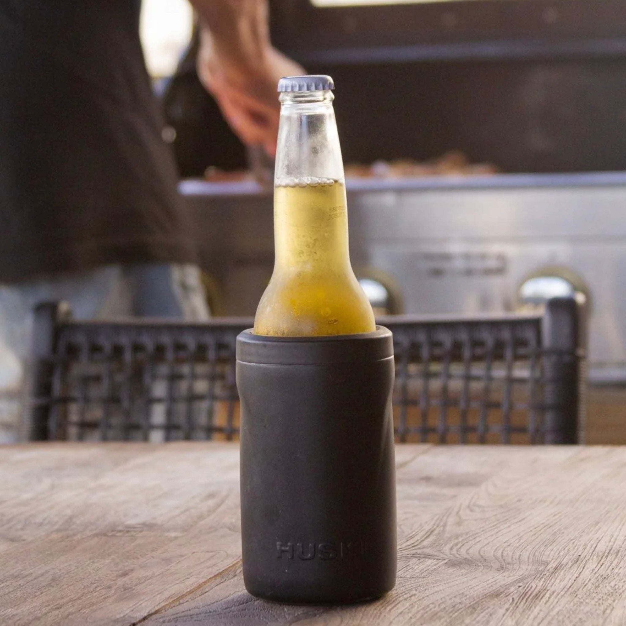 Beer bottle in a black can cooler on a wooden table with a blurred background