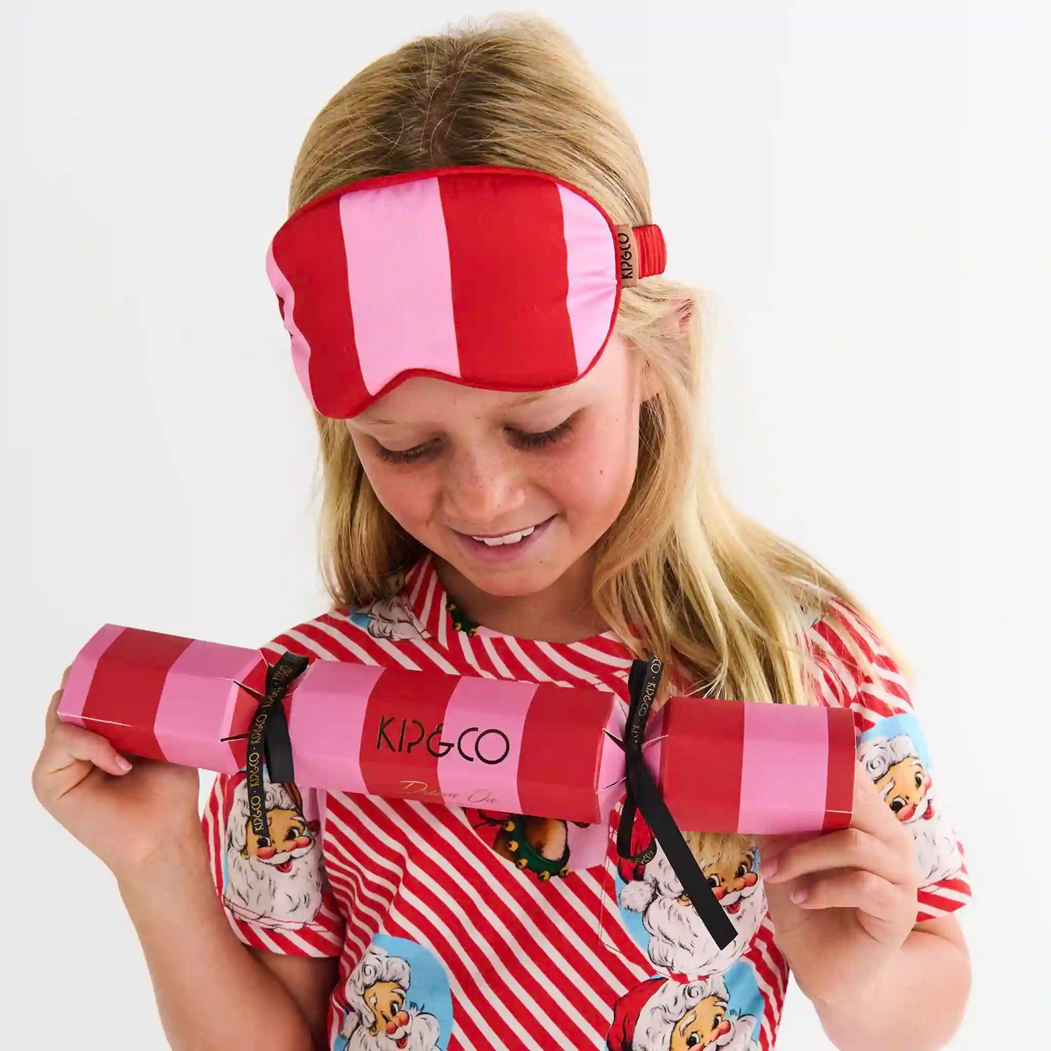 Child wearing a red and pink striped eye mask with a Kipco product in front