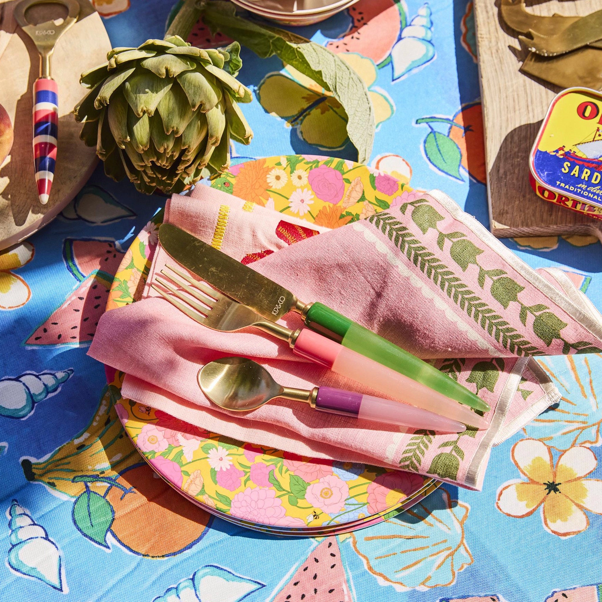 Colorful table setting with floral plates, napkins, and cutlery on a patterned tablecloth.