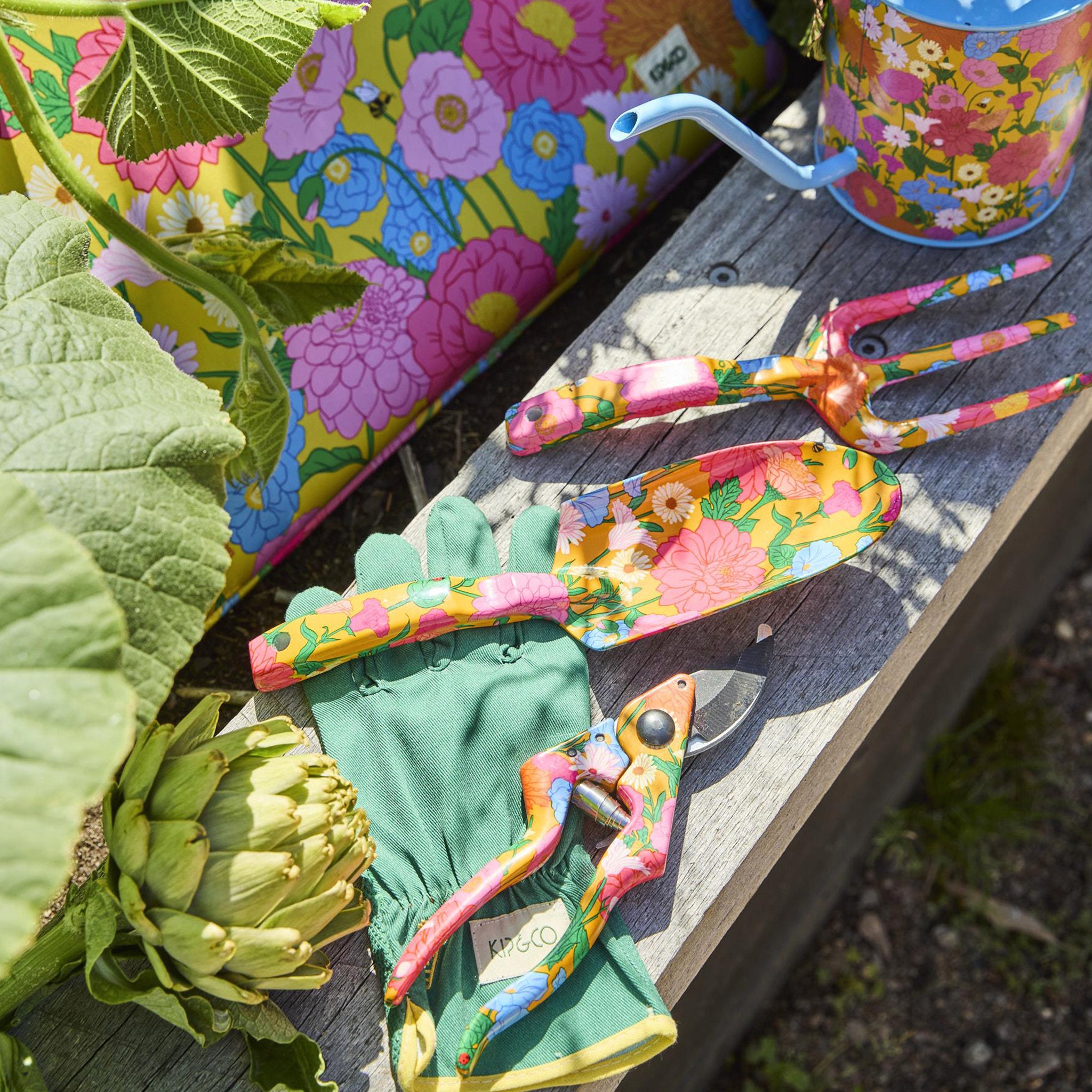 Colorful gardening tools and gloves on a wooden surface with plants in the background
